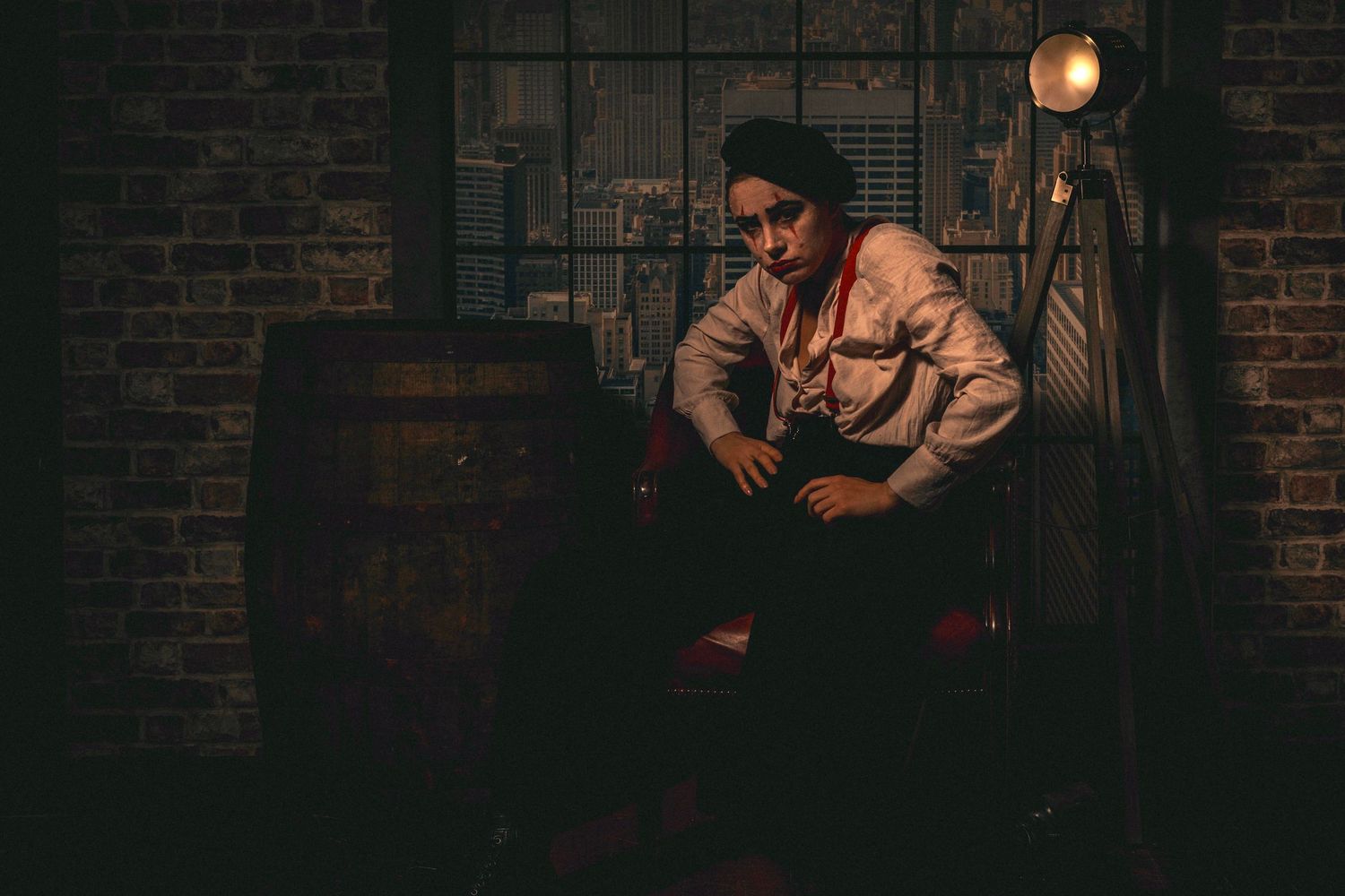 A person in a dimly lit industrial setting sits near a barrel, wearing a white shirt with dramatic lighting.