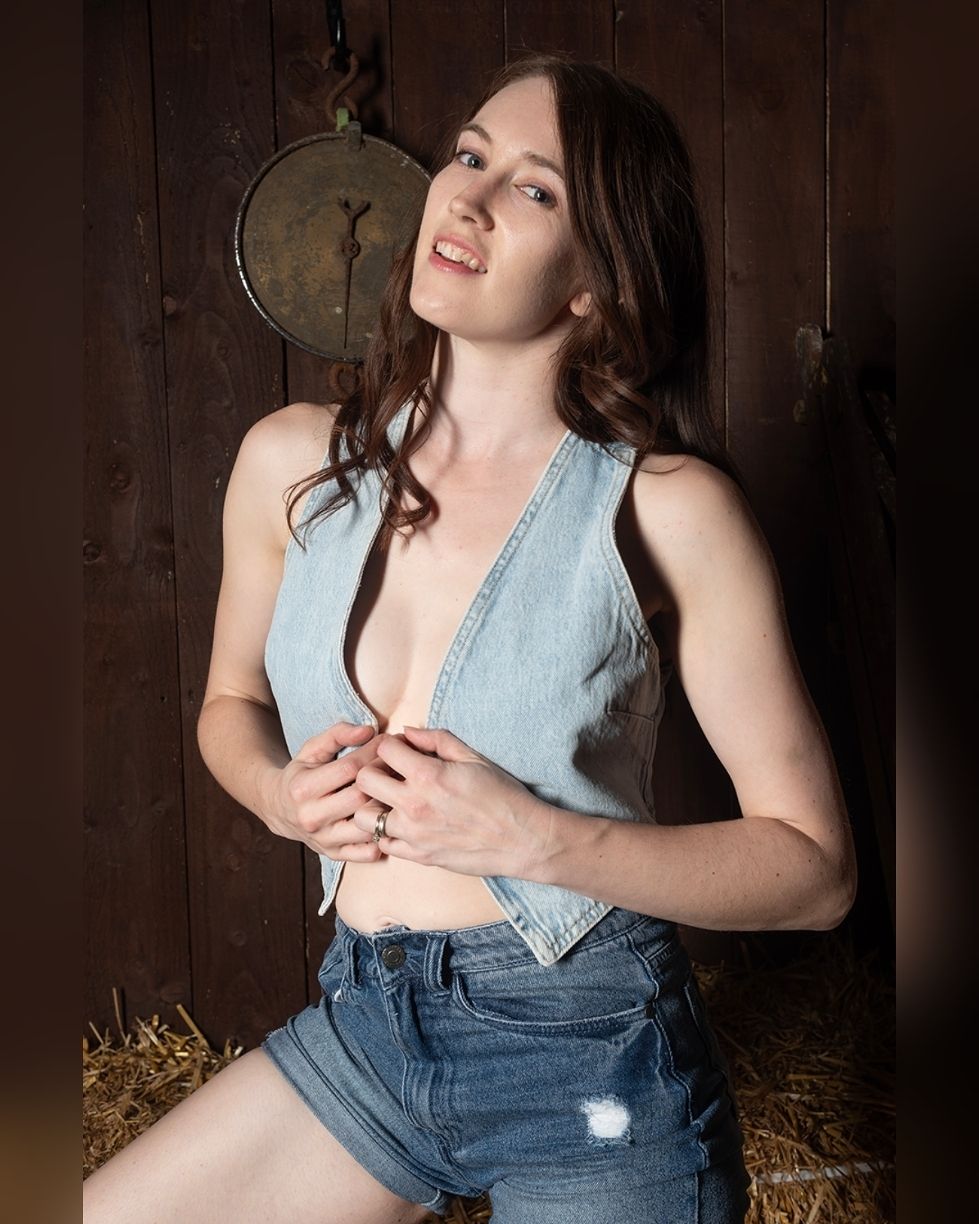 A young woman with long dark hair is smiling and posing in front of a wooden background.