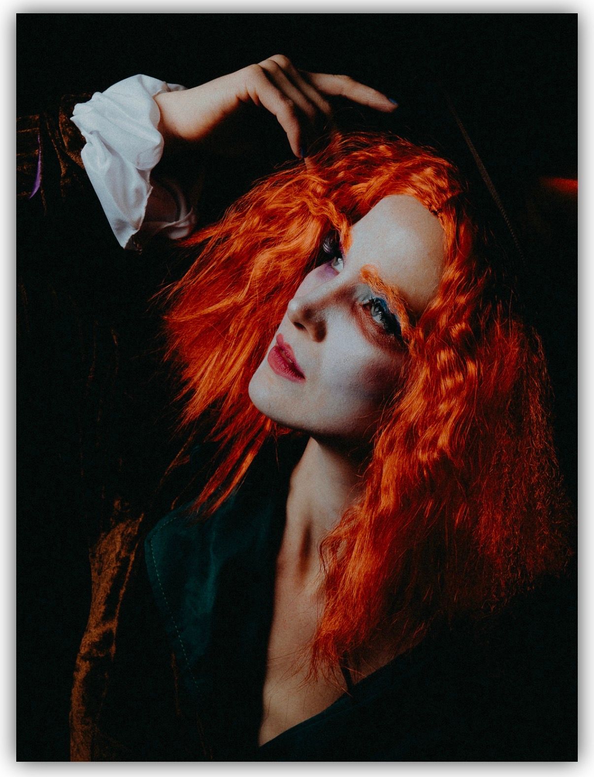 Dramatic portrait featuring vibrant red hair against dark background with moody artistic lighting.
