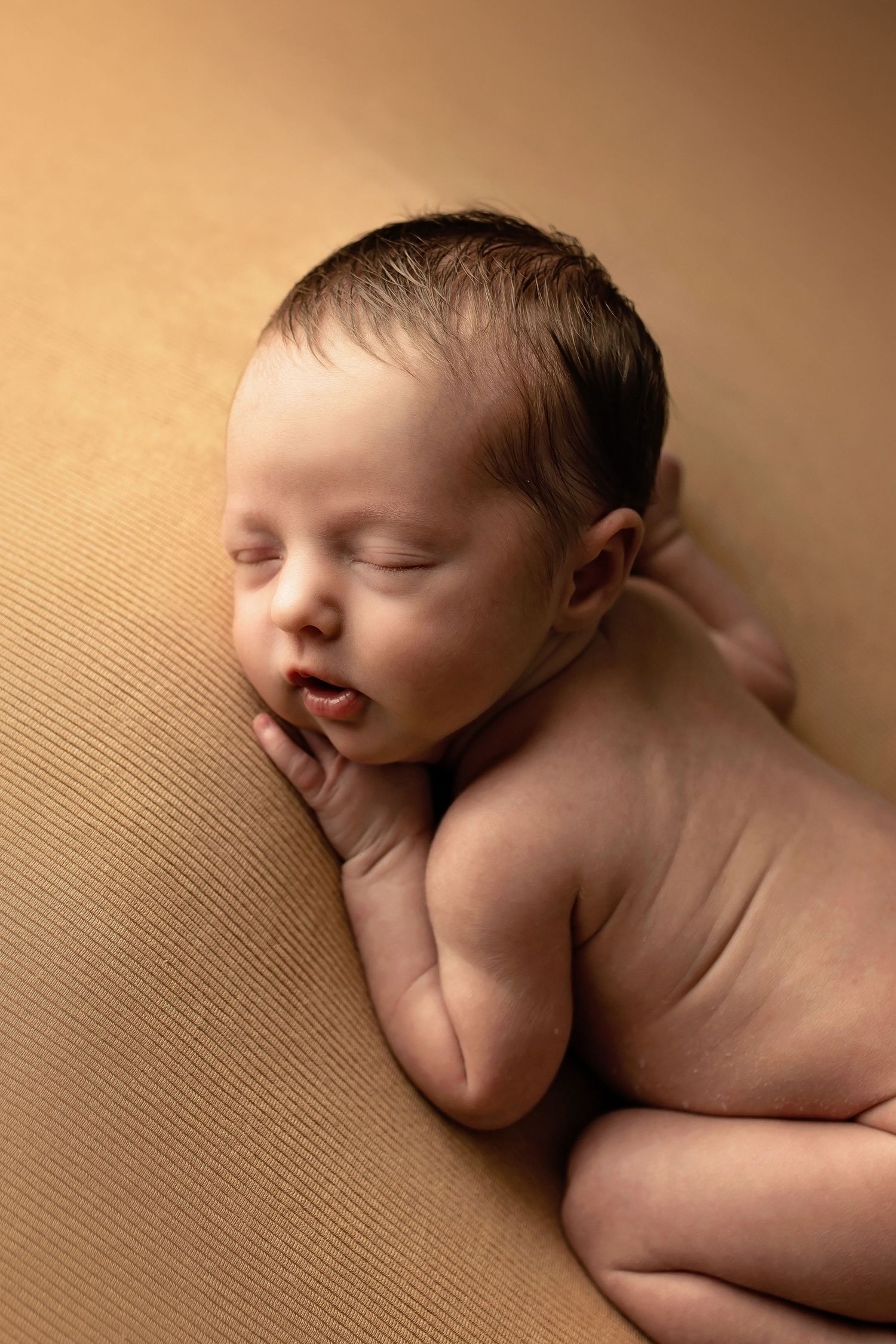 Minimalist newborn photography series showing a sleeping baby against a textured brown background.