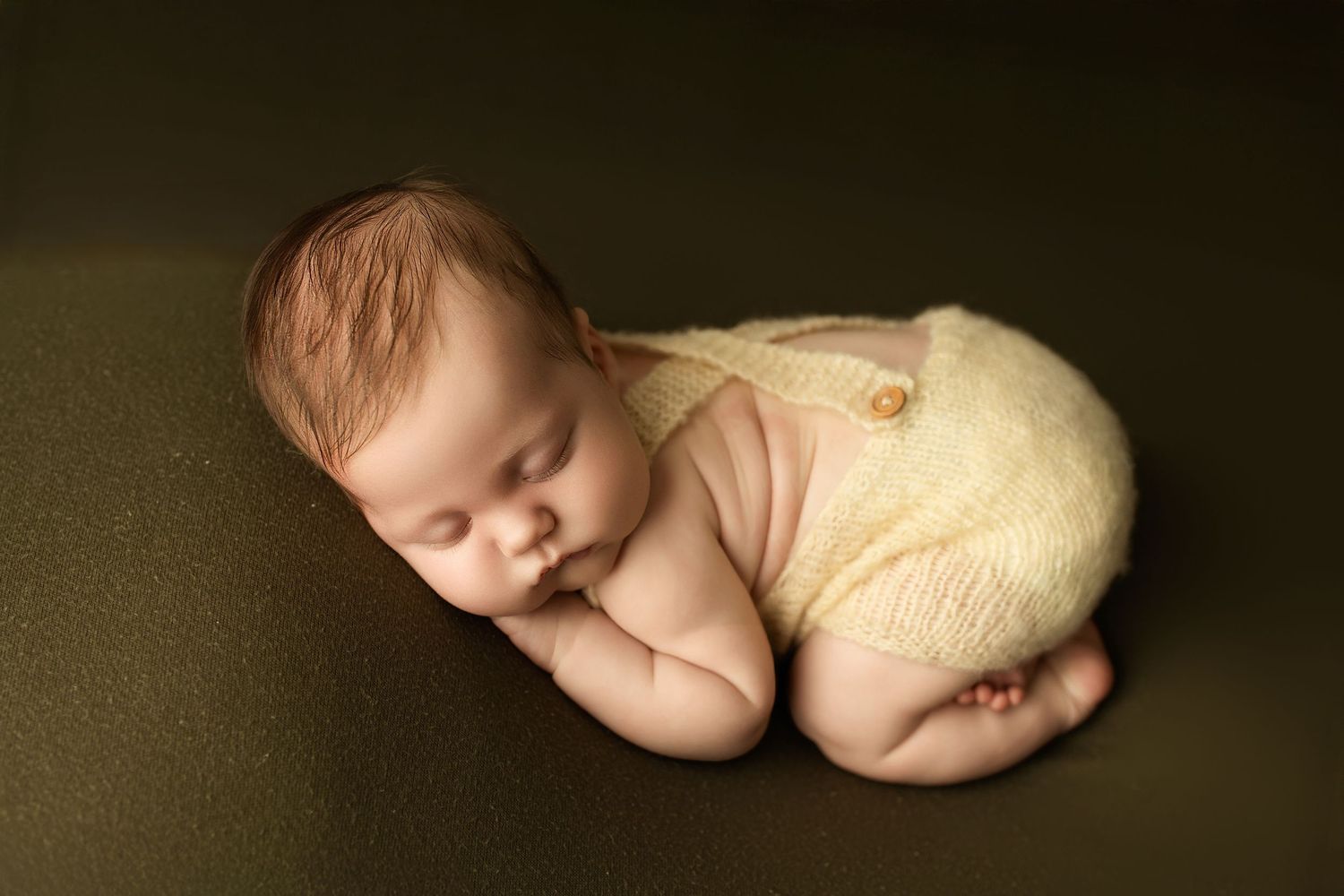 Peaceful sleeping newborn in yellow wrap on dark green background.