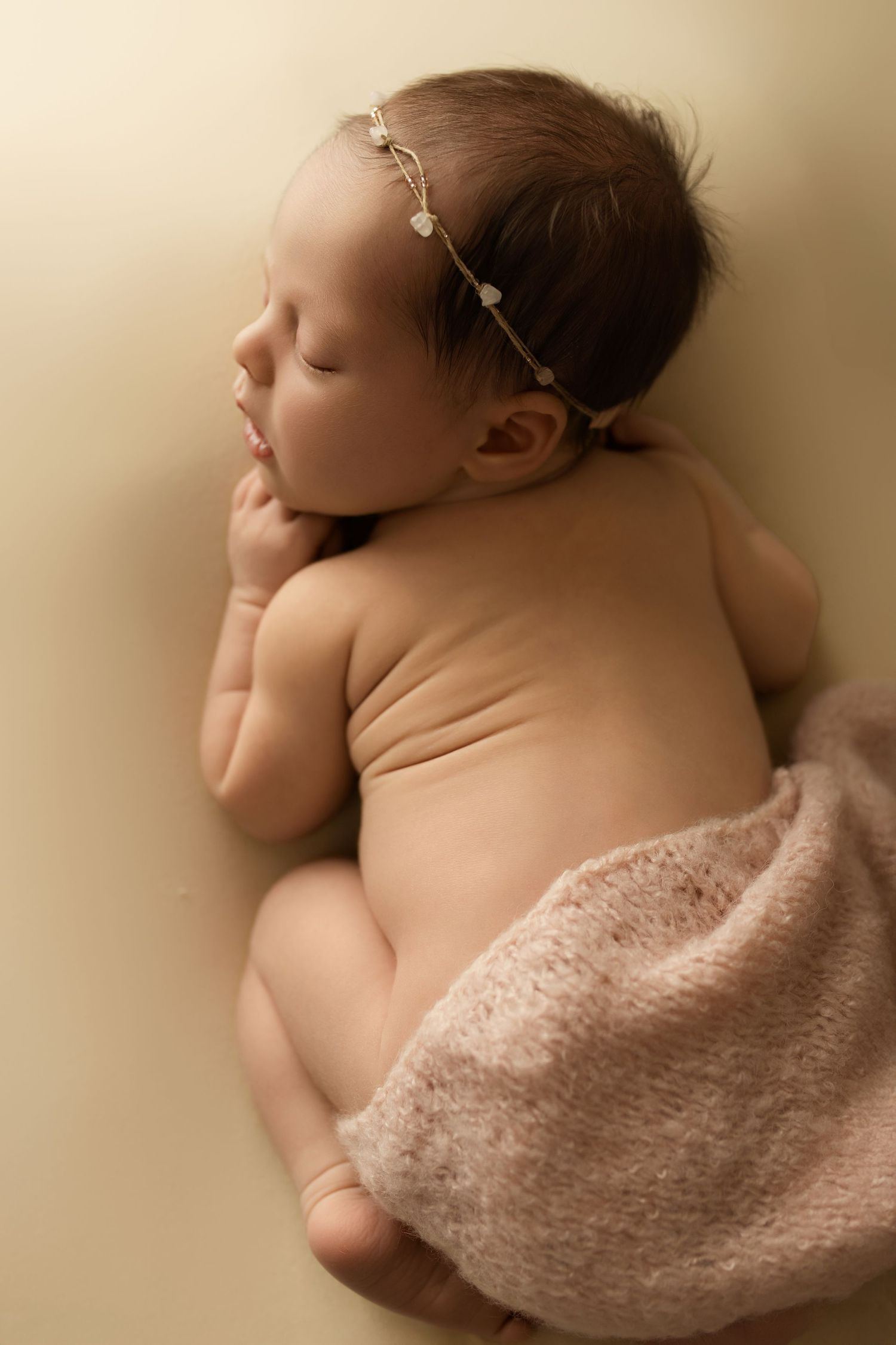 A series of artistic newborn photos showing a sleeping baby wrapped in soft pink fabric on a simple beige backdrop.