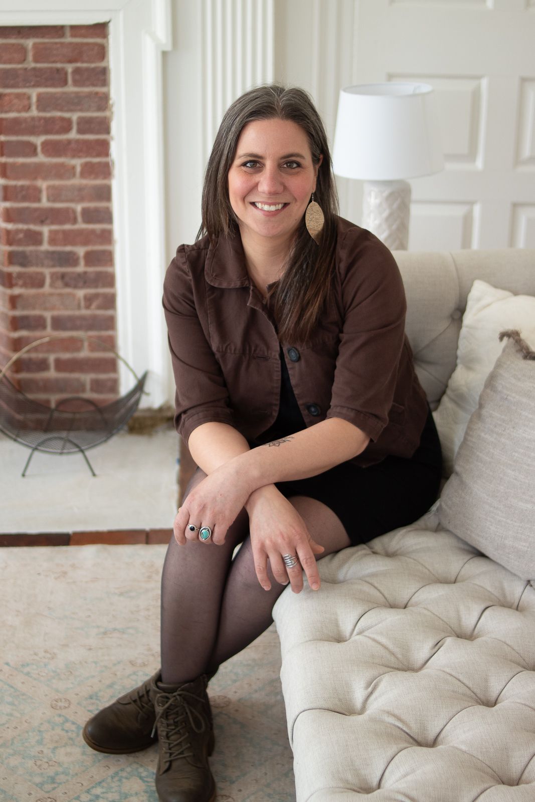 Professional portrait on cream tufted sofa wearing brown jacket and boots.