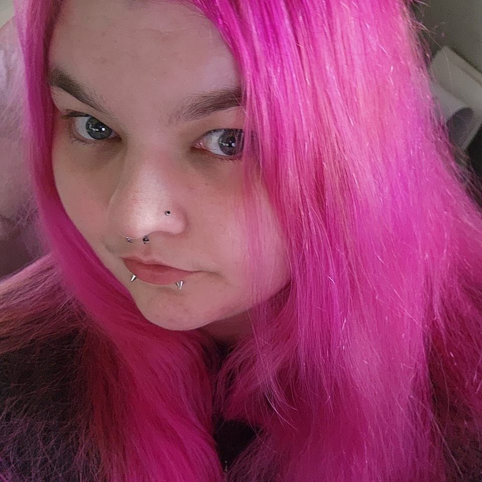 A person with vibrant hot pink hair gazes at the camera in a close-up selfie shot.