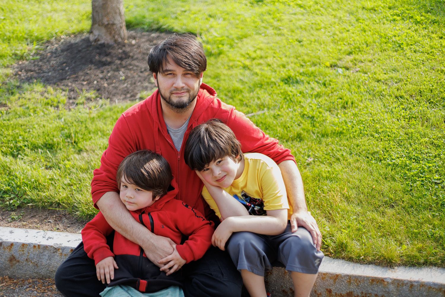 A sequence of loving family moments captured on grass shows parents and children embracing in casual outdoor settings.