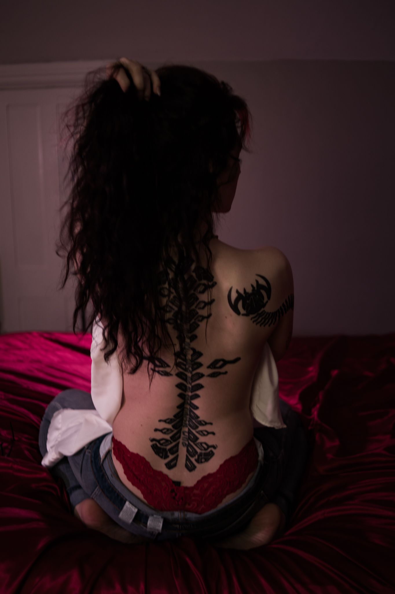 A tree branch tattoo design appears prominently on the back of someone wearing denim against dark moody lighting.