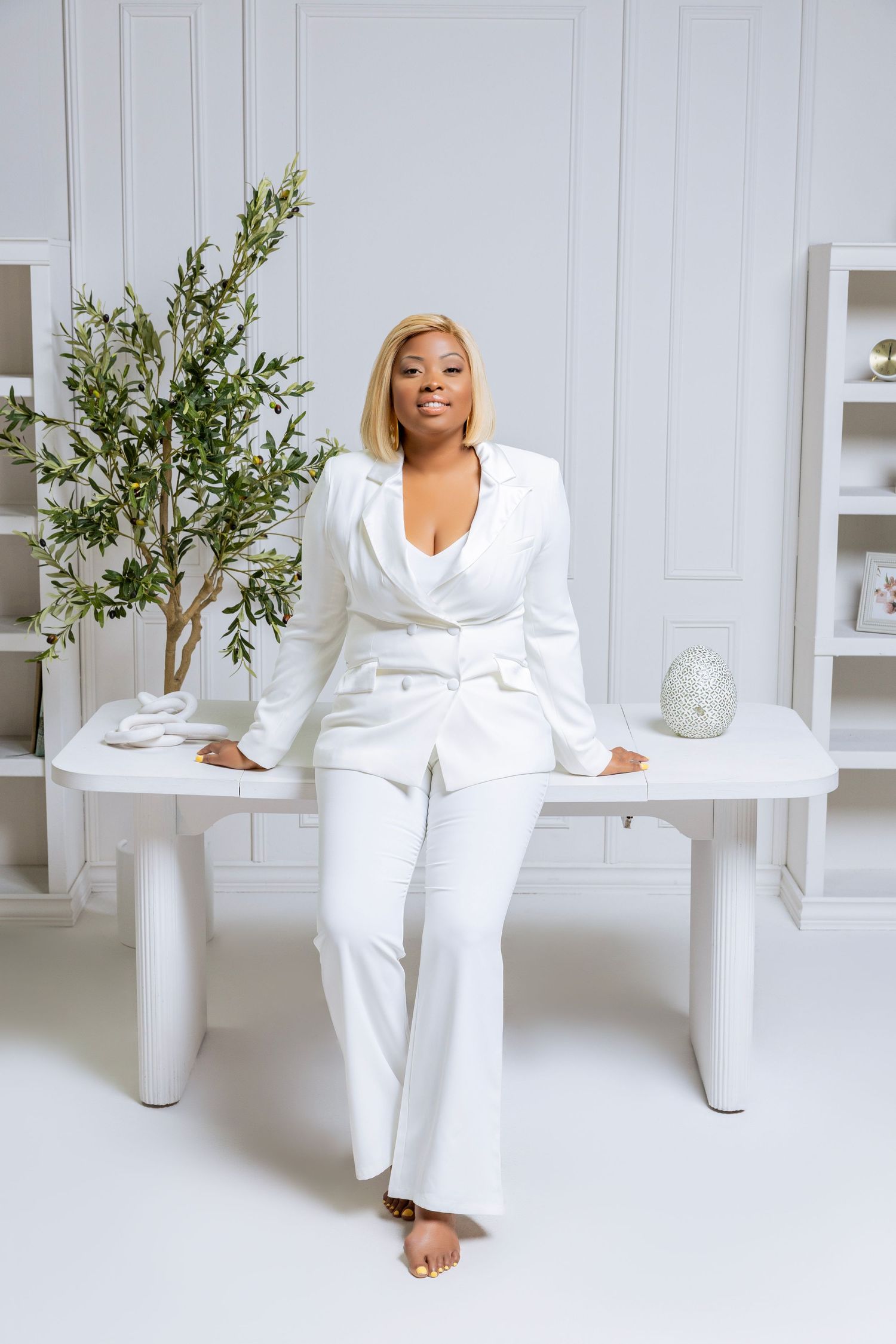 Person wearing crisp white ensemble lounges elegantly on minimalist furniture in a bright, modern studio setting.