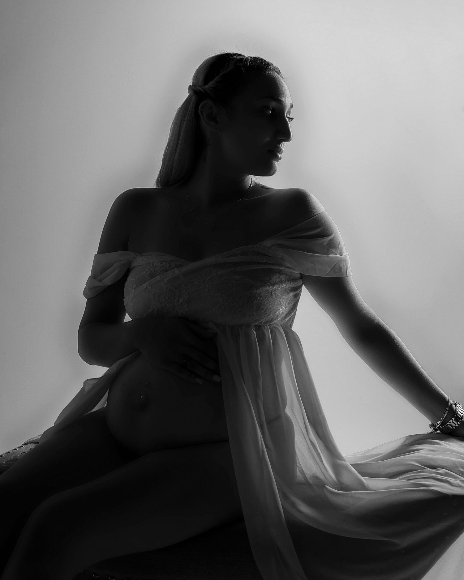 Silhouette of a figure in an off-shoulder white dress sits in contemplative profile against a light background.