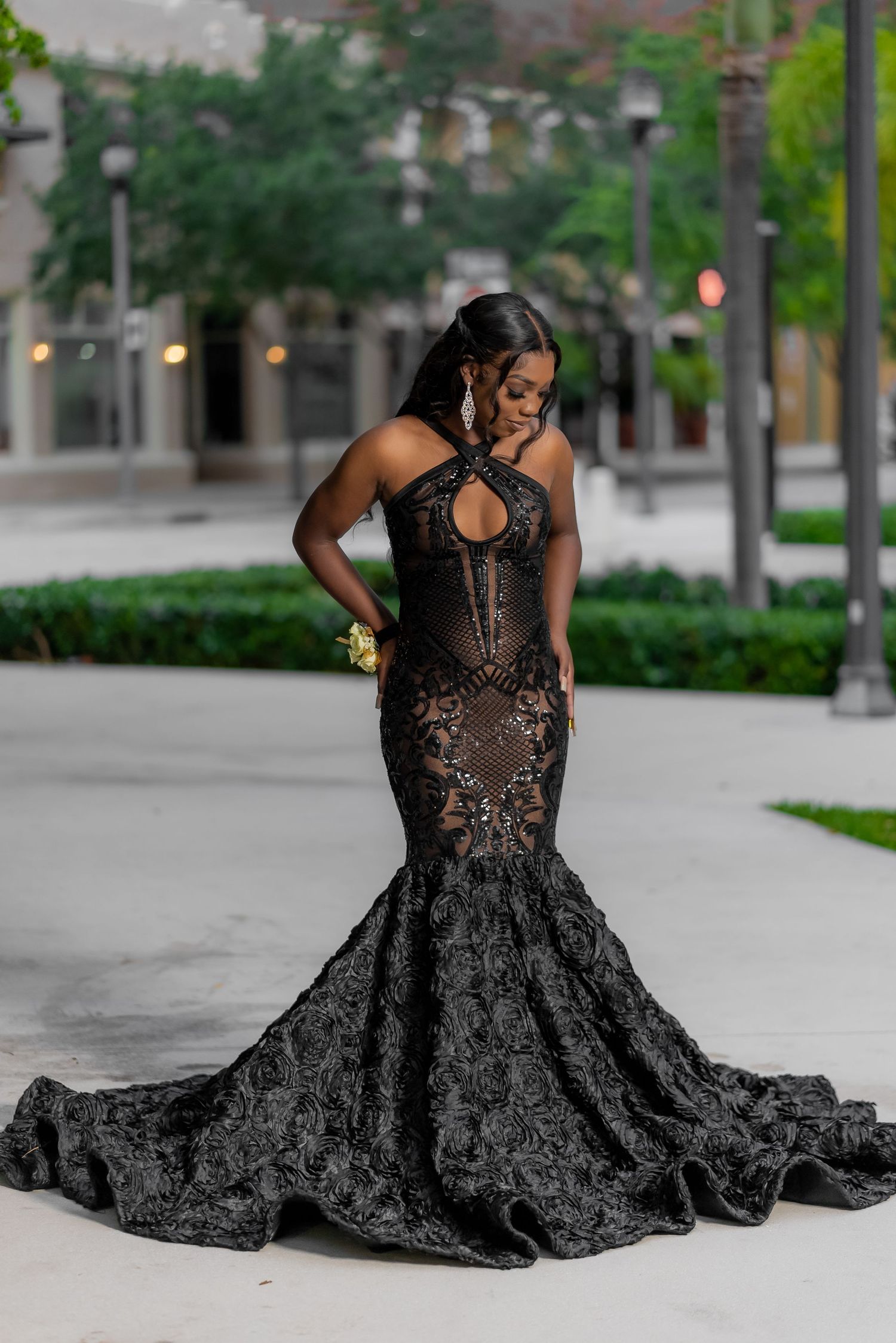 Elegant black mermaid gown with lace details and keyhole neckline features dramatic train on urban pathway at dusk.