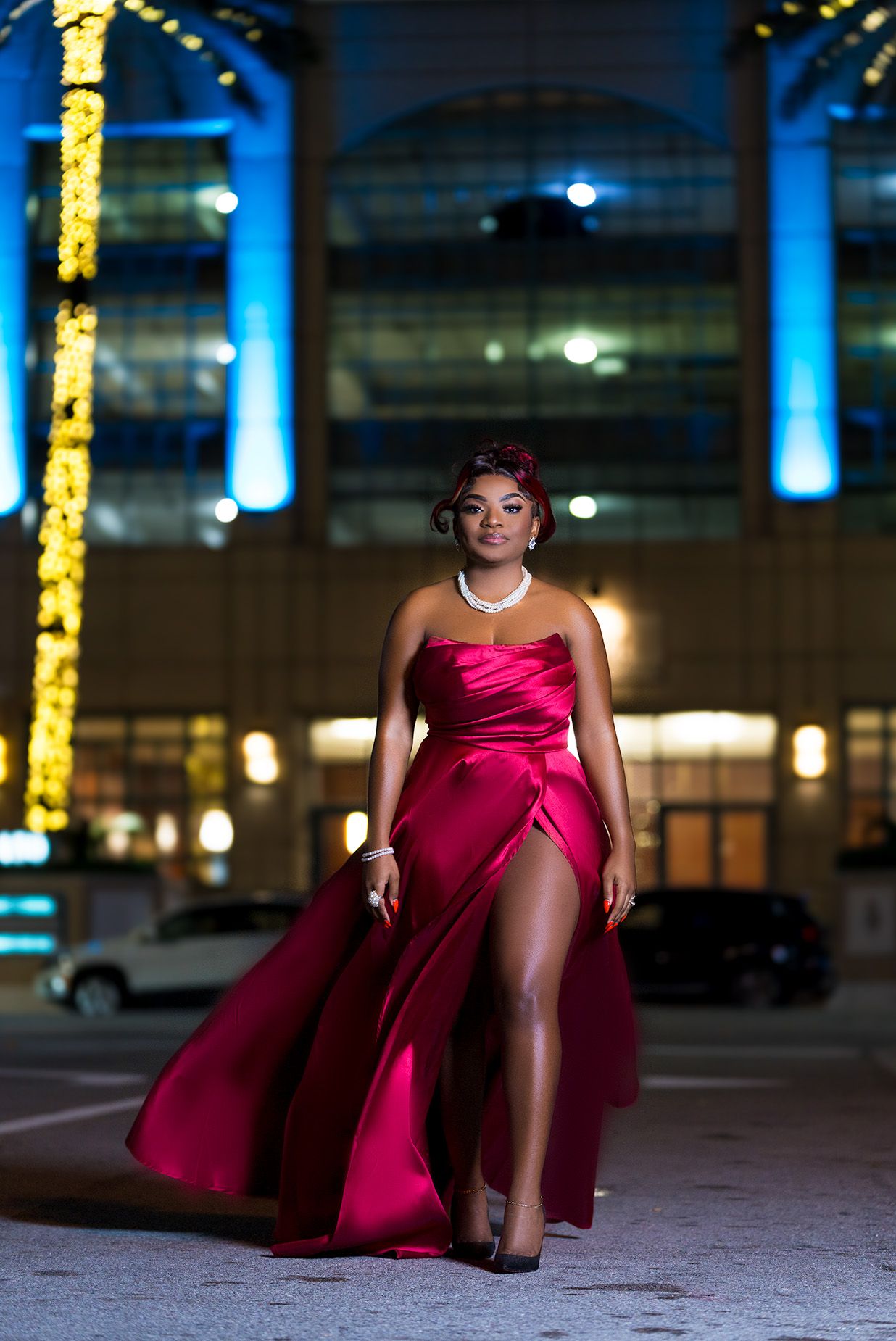 Dramatic nighttime fashion portrait in red dress with contrasting blue and yellow lighting in an urban setting.