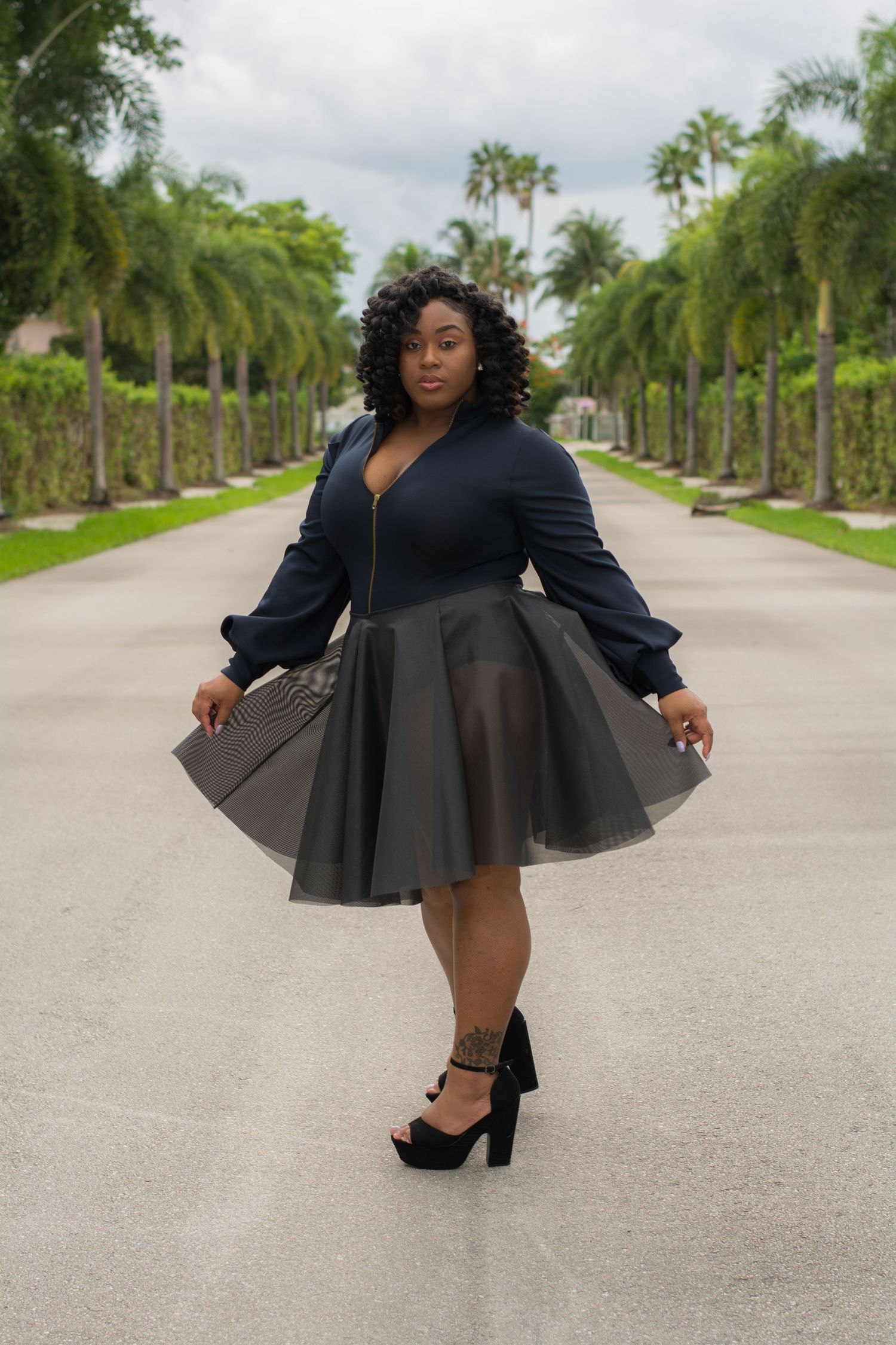 A stylish outfit featuring a black dress with full skirt and balloon sleeves photographed on a palm tree-lined path.