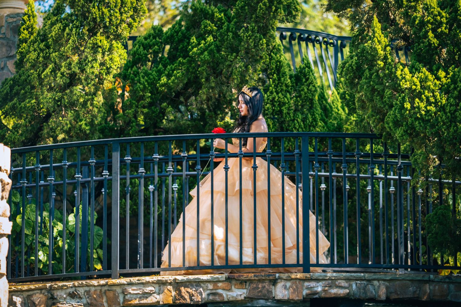 Two people sharing a kiss on an ornate bridge railing decorated with locks in front of lush green foliage.