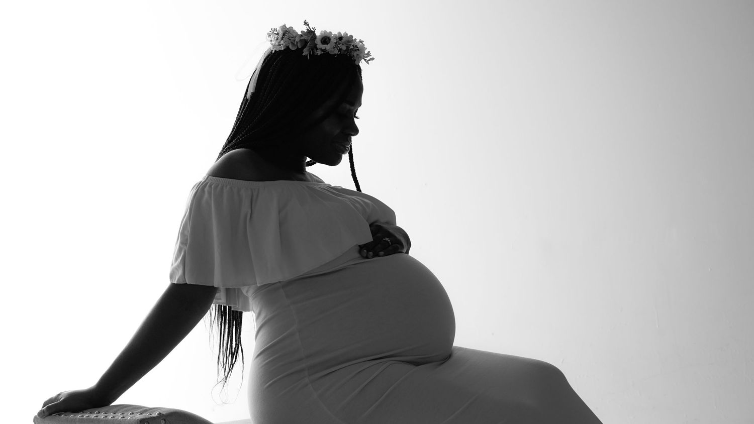 Black and white silhouette photo of an expectant mother sitting in side profile against a light background.