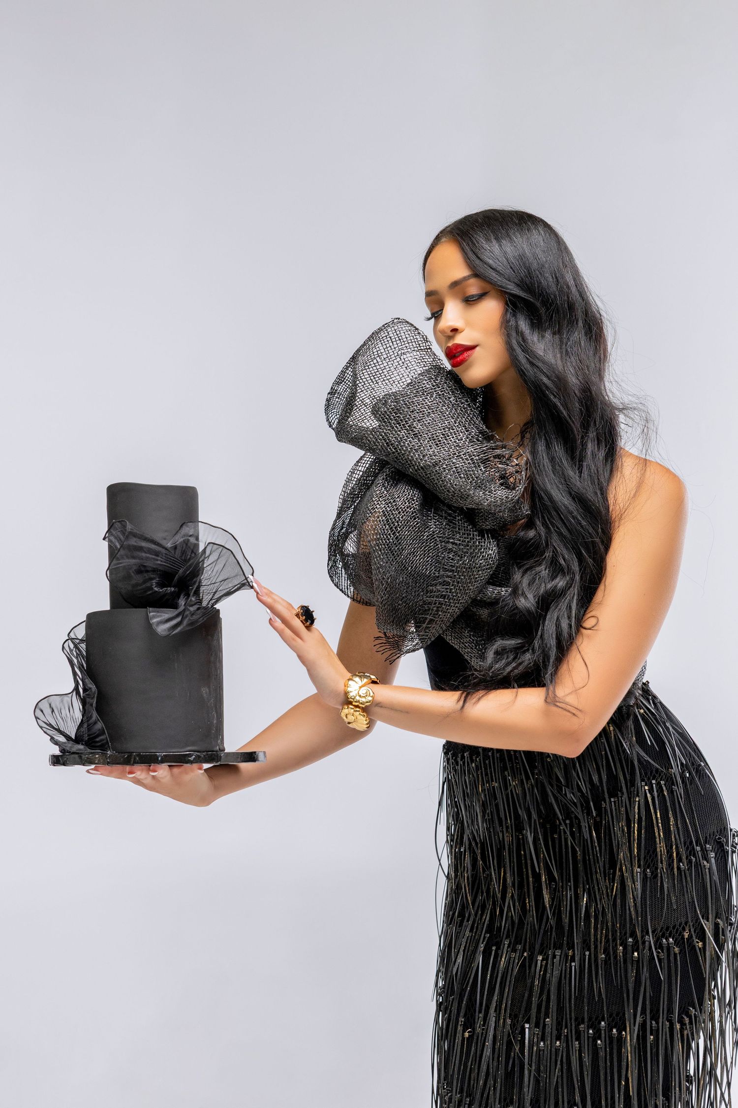 Gothic black tiered cake with dark tulle accents and fringe details photographed in multiple angles on light background.