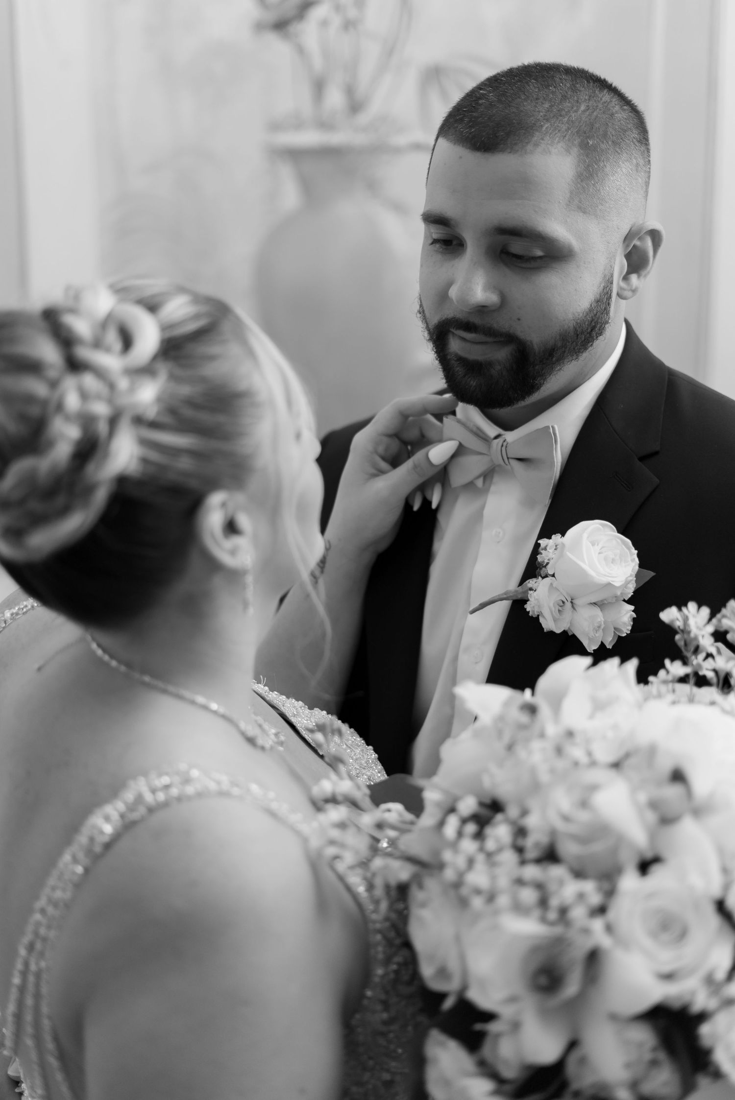 A tender moment at a wedding with a bowtie adjustment and floral bouquet in black and white photography.