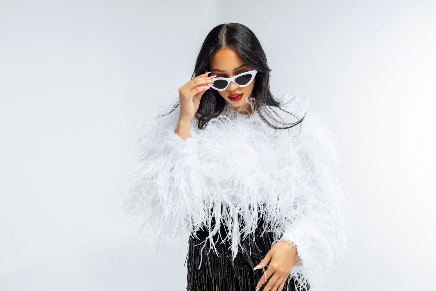 Model in feathered white top and sunglasses poses against white background.
