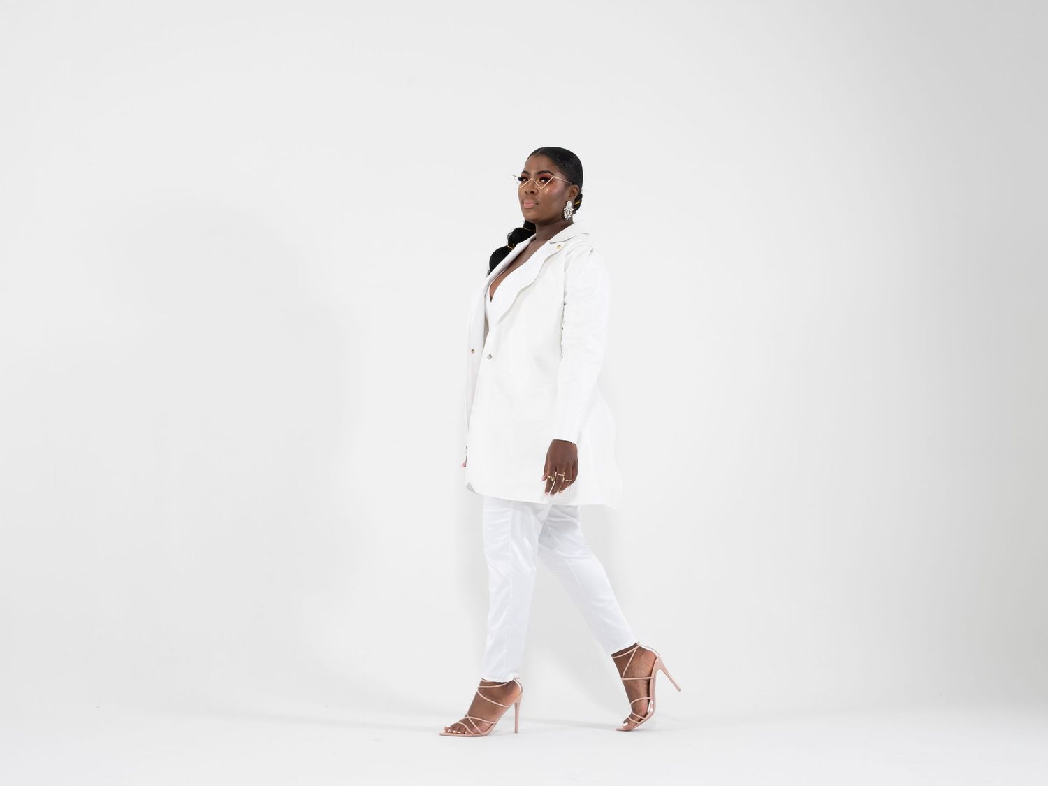 Professional wearing an all-white business suit with matching heels stands elegantly against a light background.