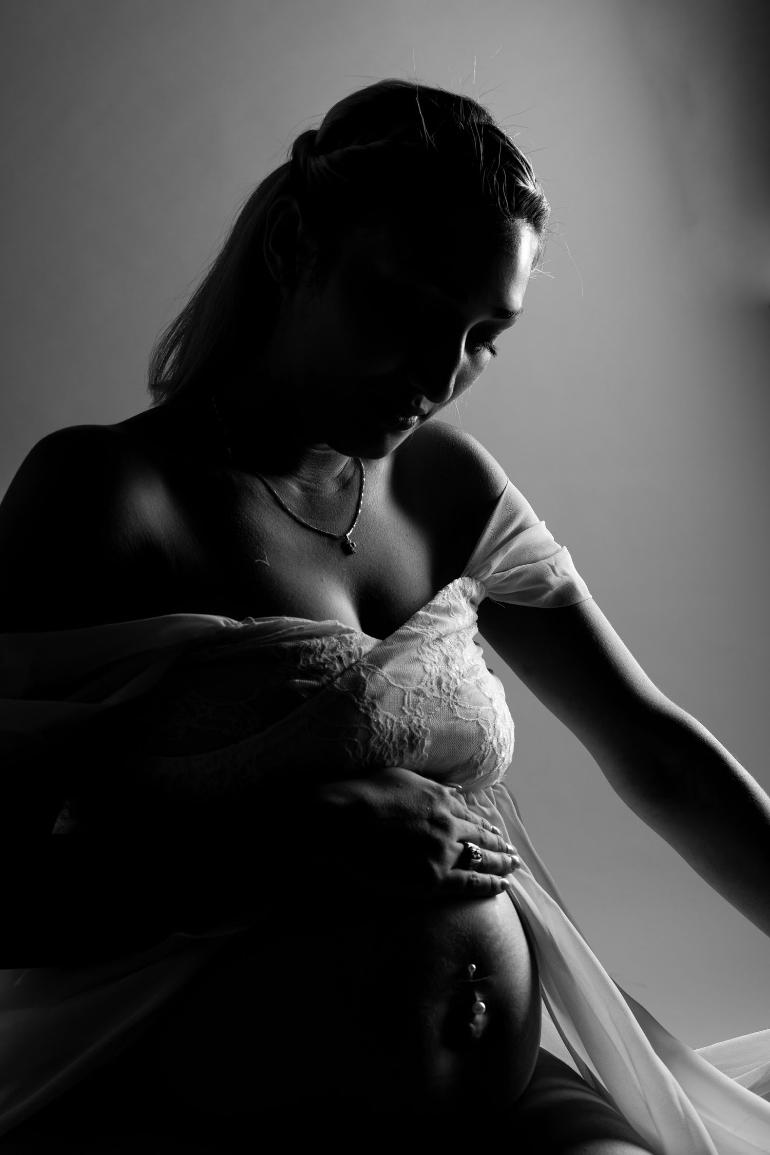 Black and white artistic maternity photo showing a silhouette in lace against dramatic lighting.