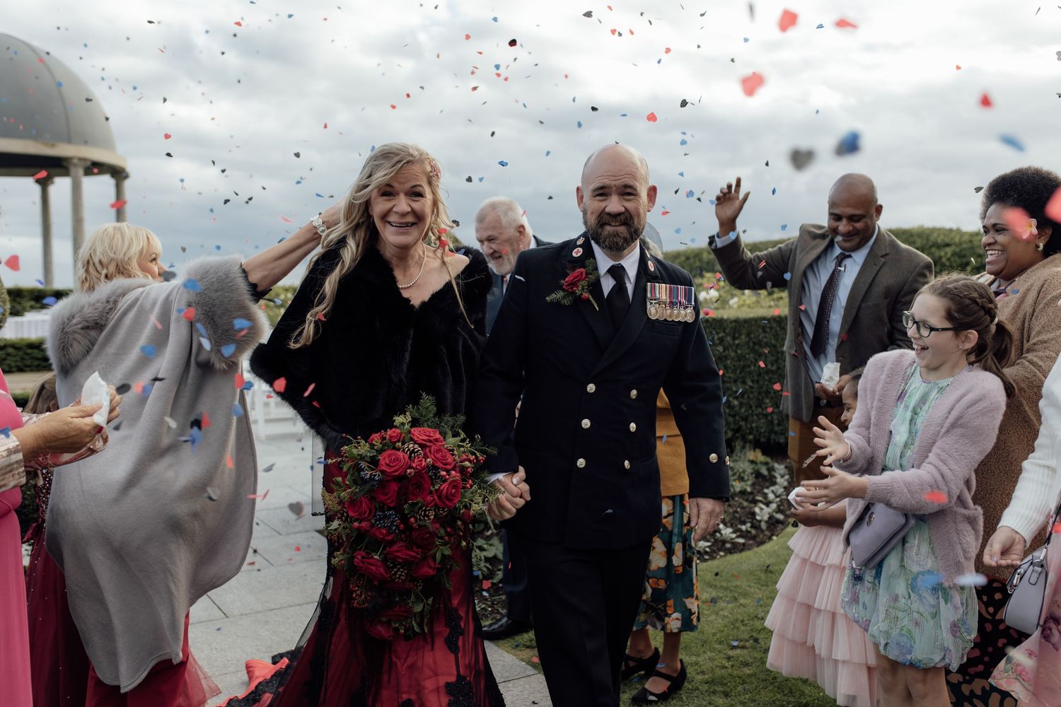 Wedding guests throw pink and white confetti in celebration during an outdoor ceremony.