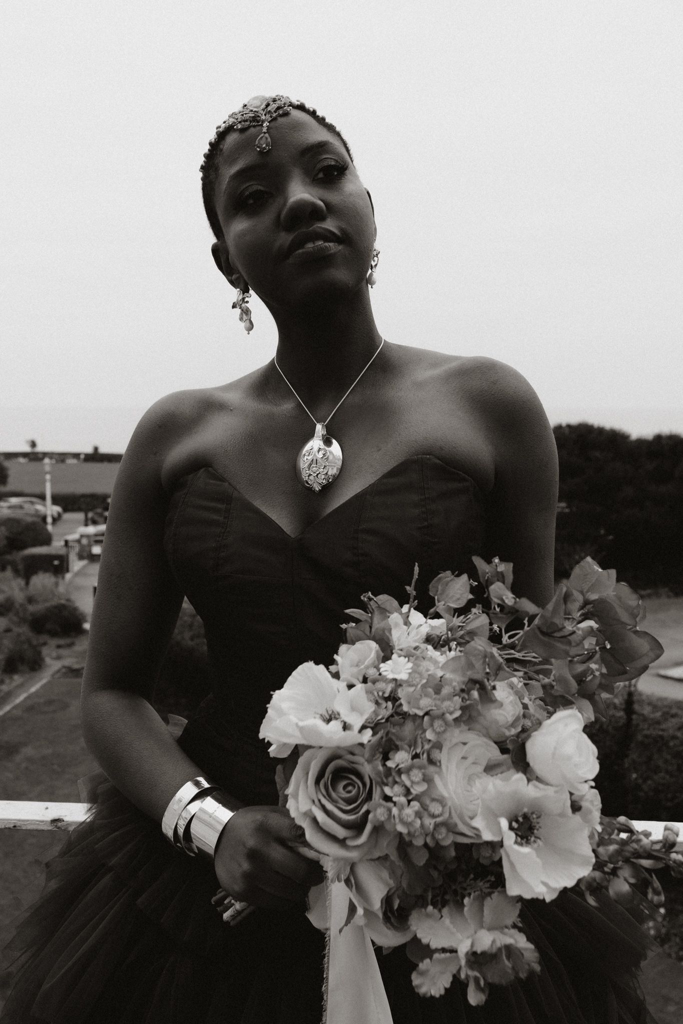 Black and white photo of a bride in a strapless dress holding a bouquet of roses and white flowers.