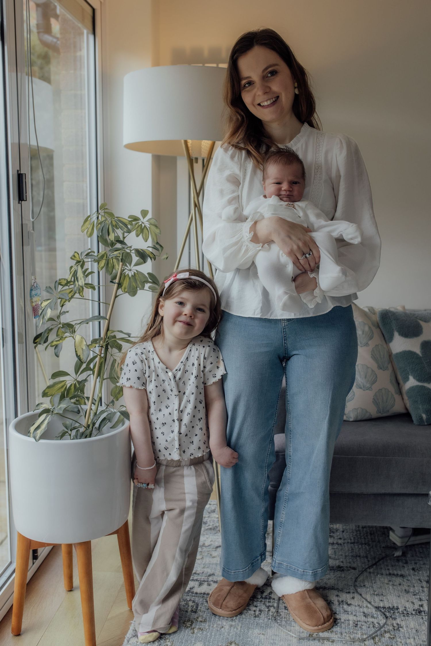 Family members in casual attire stand together in a bright living room with houseplants and modern decor.