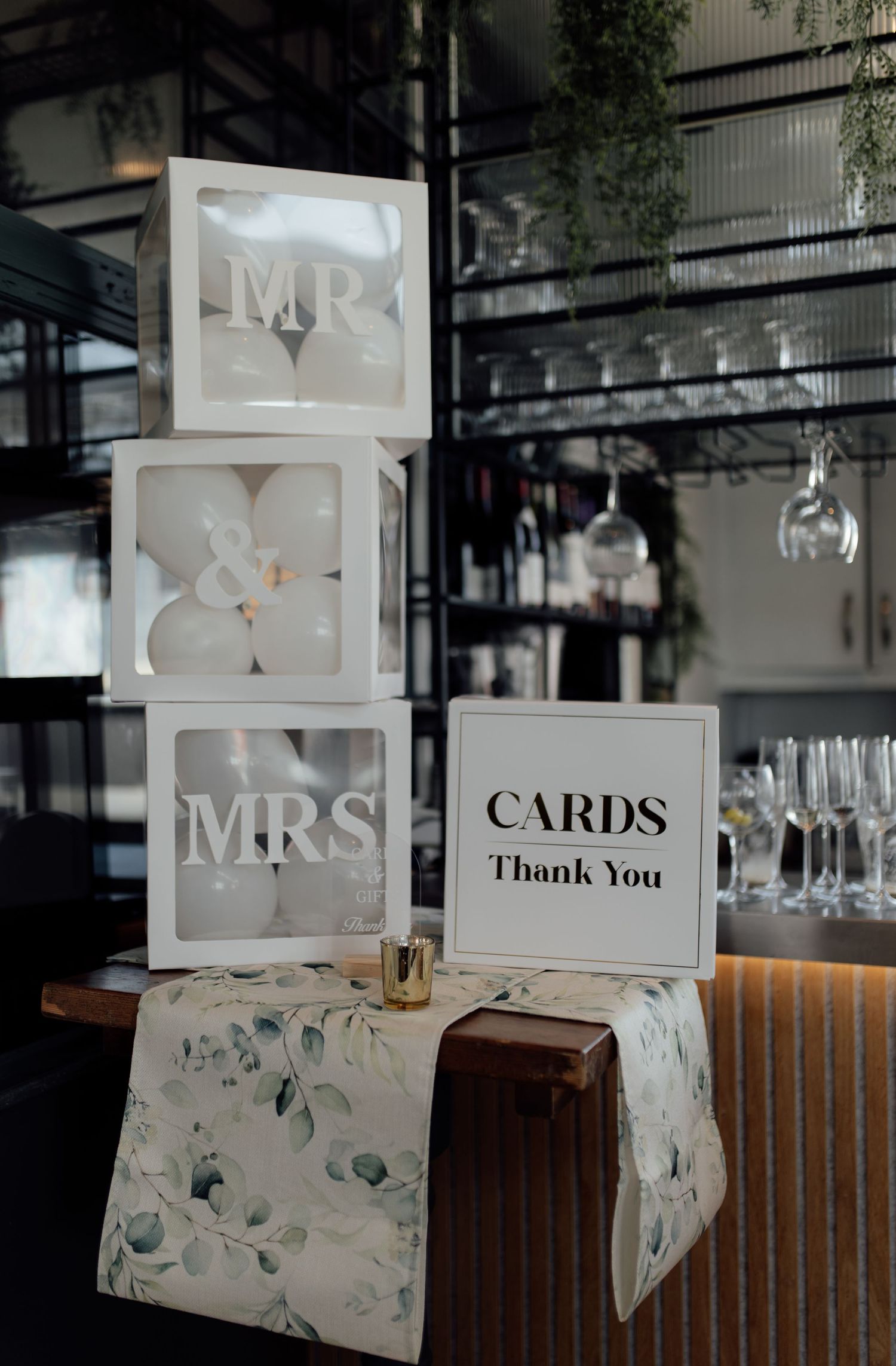 White wedding card boxes with 'Mr & Mrs' text and floral decorations displayed on wooden table at reception venue.
