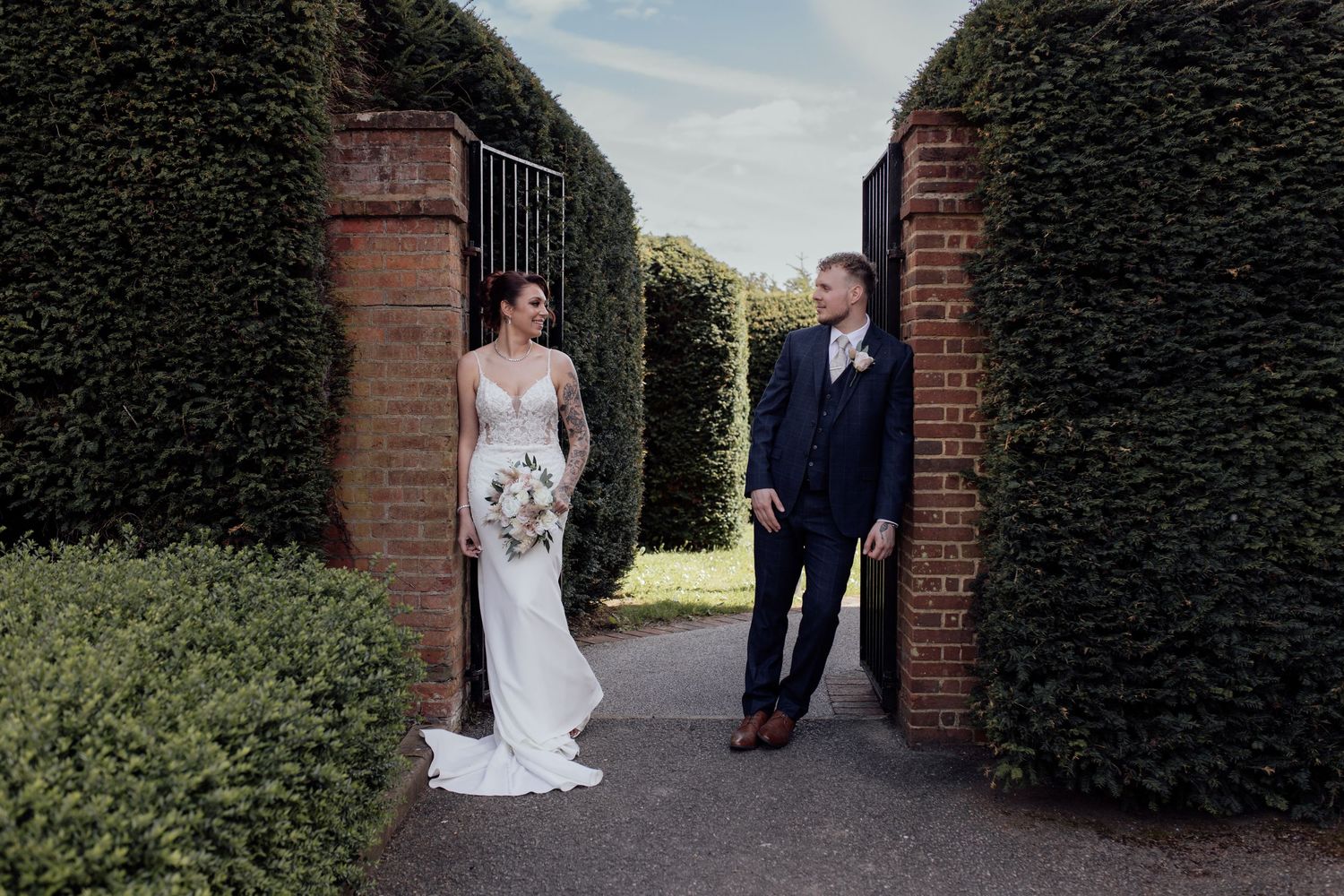 Bride and groom stand by a gate way looking at each other
