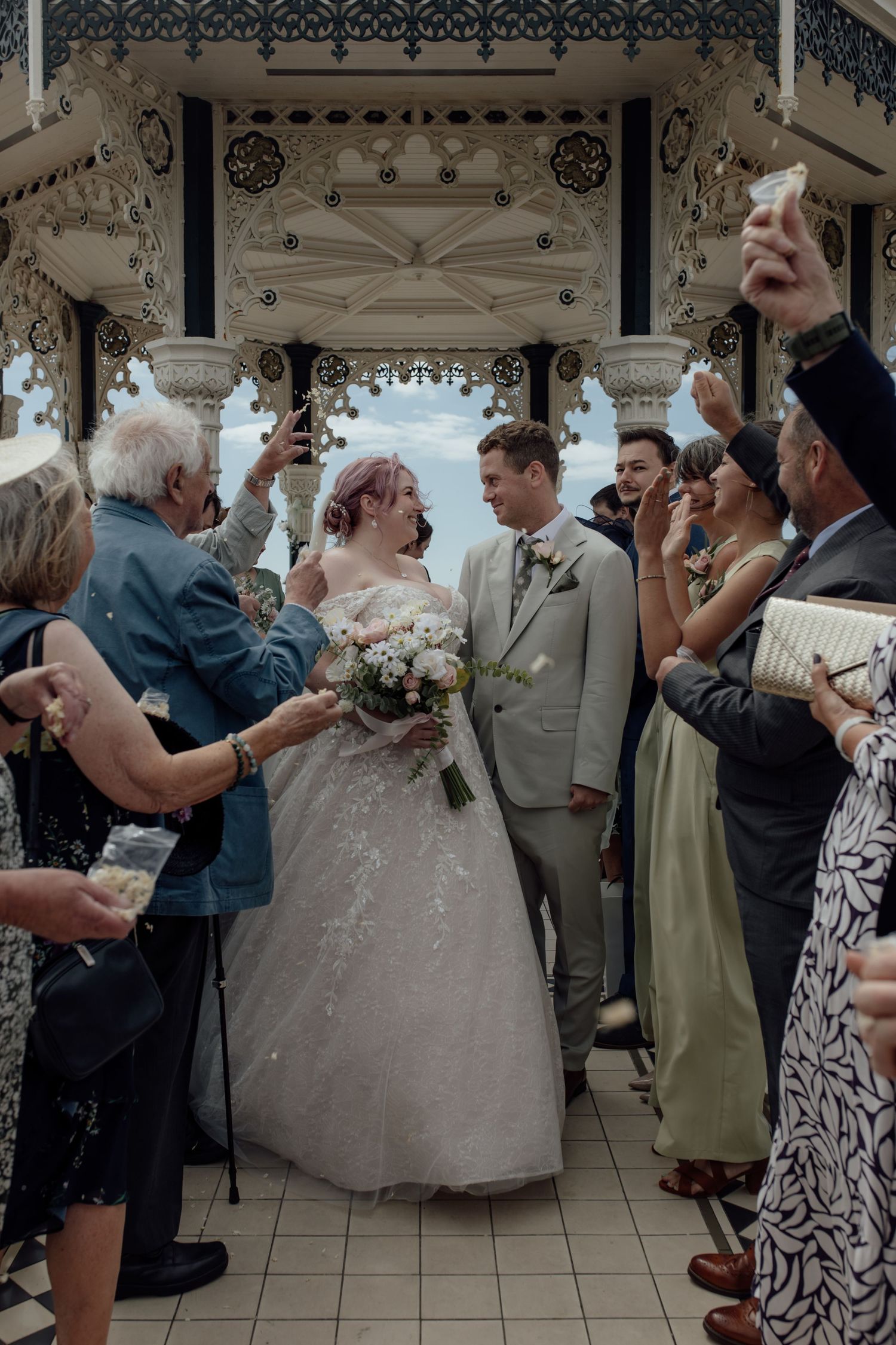 Wedding guests dance and celebrate on the dance floor at a reception venue with ornate white decorative ceiling details.