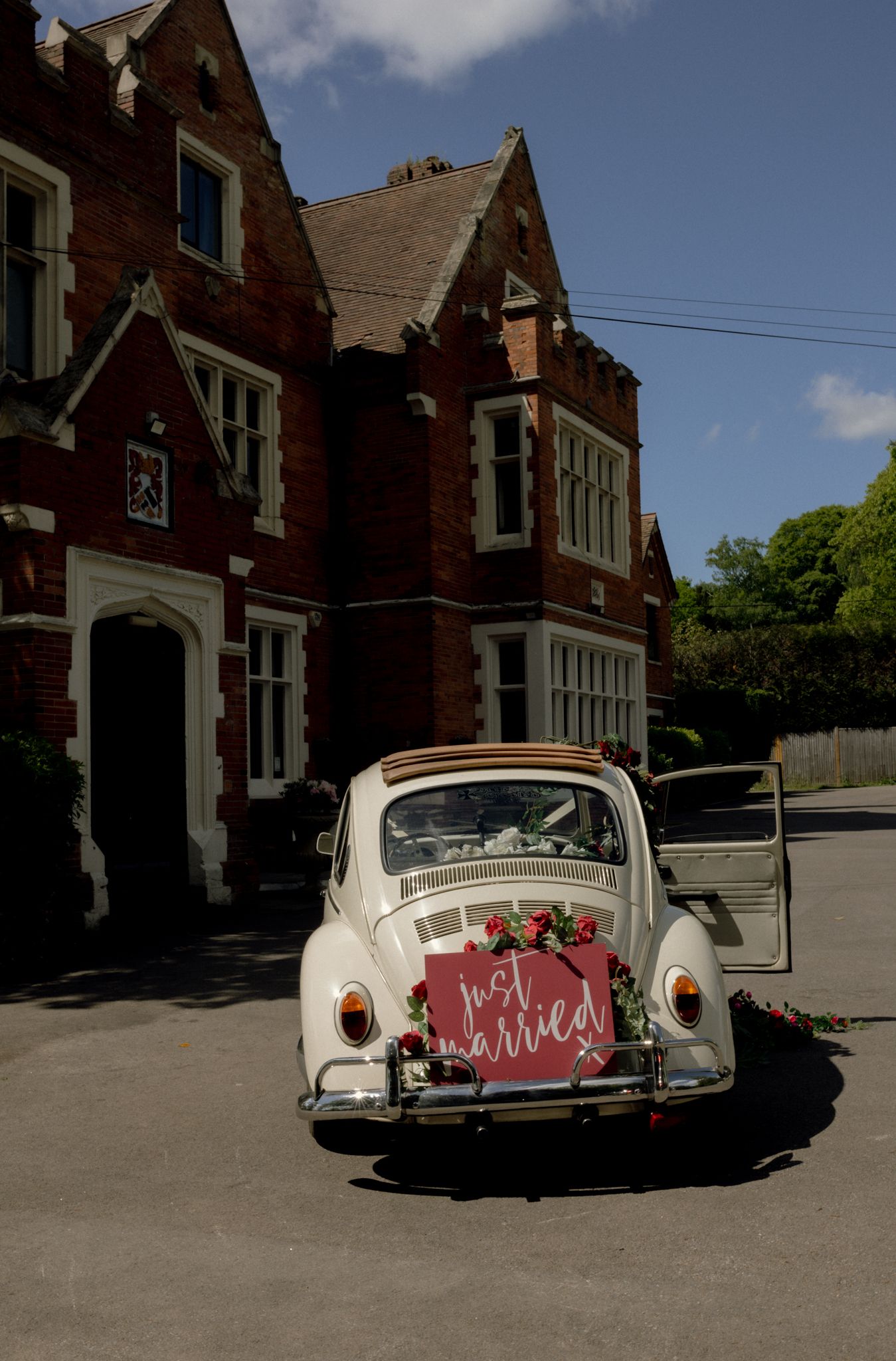 Classic white vintage wedding car decorated with 'just married' sign parked outside brick building.