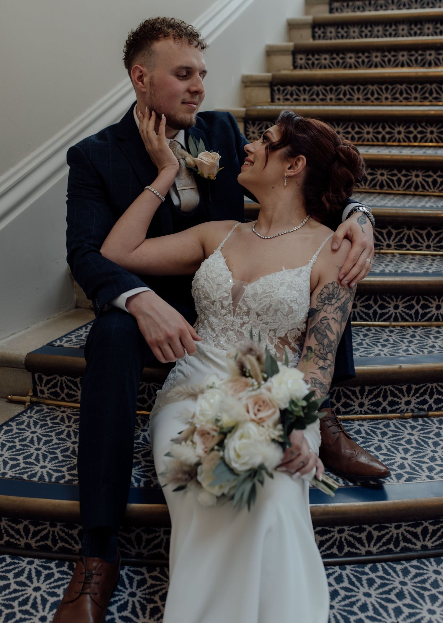 Bride and groom sit on stairs holding and looking at each other.