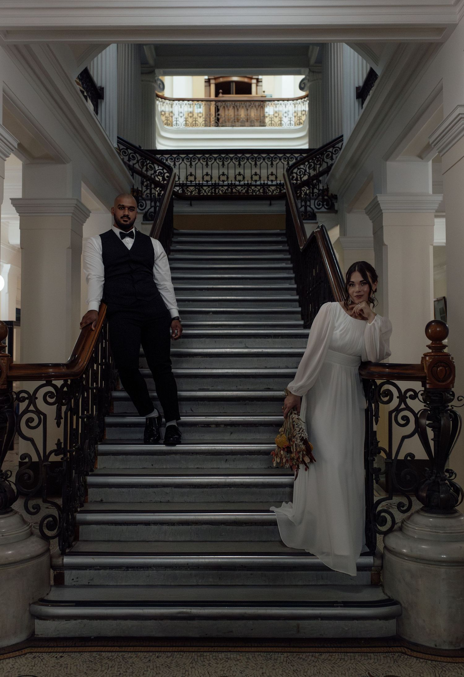 A sequence of wedding photos showing a couple descending an elegant staircase with ornate iron railings in a grand interior.