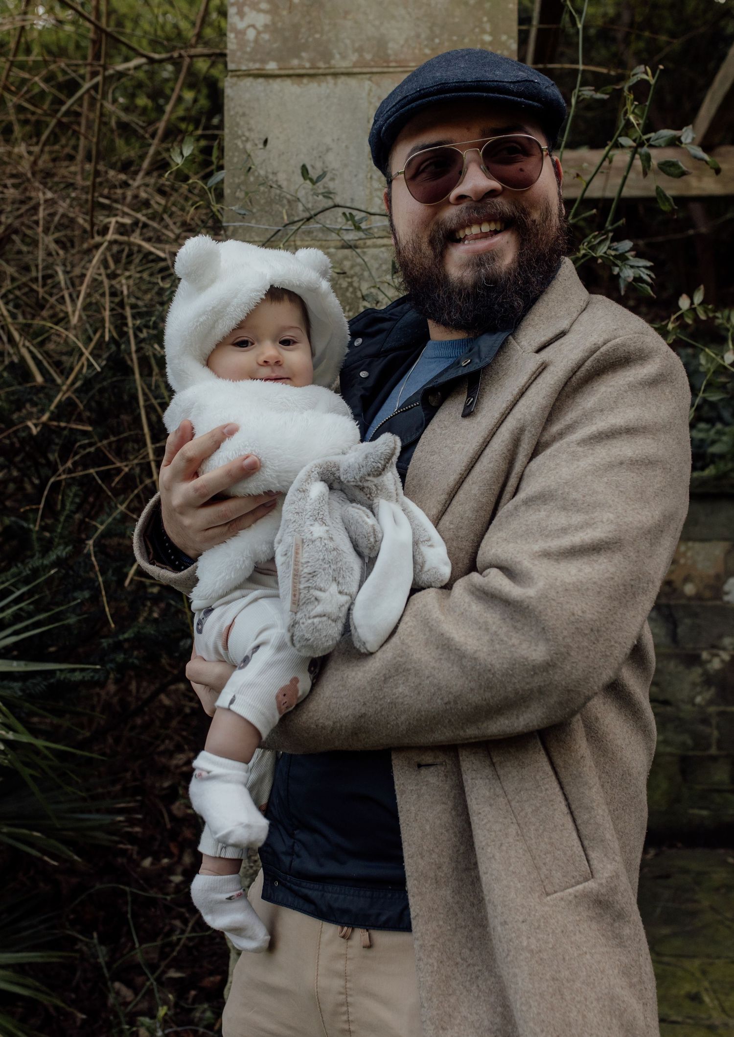 A series of photos showing a person in a beige coat holding a baby dressed in white winter clothing outdoors.