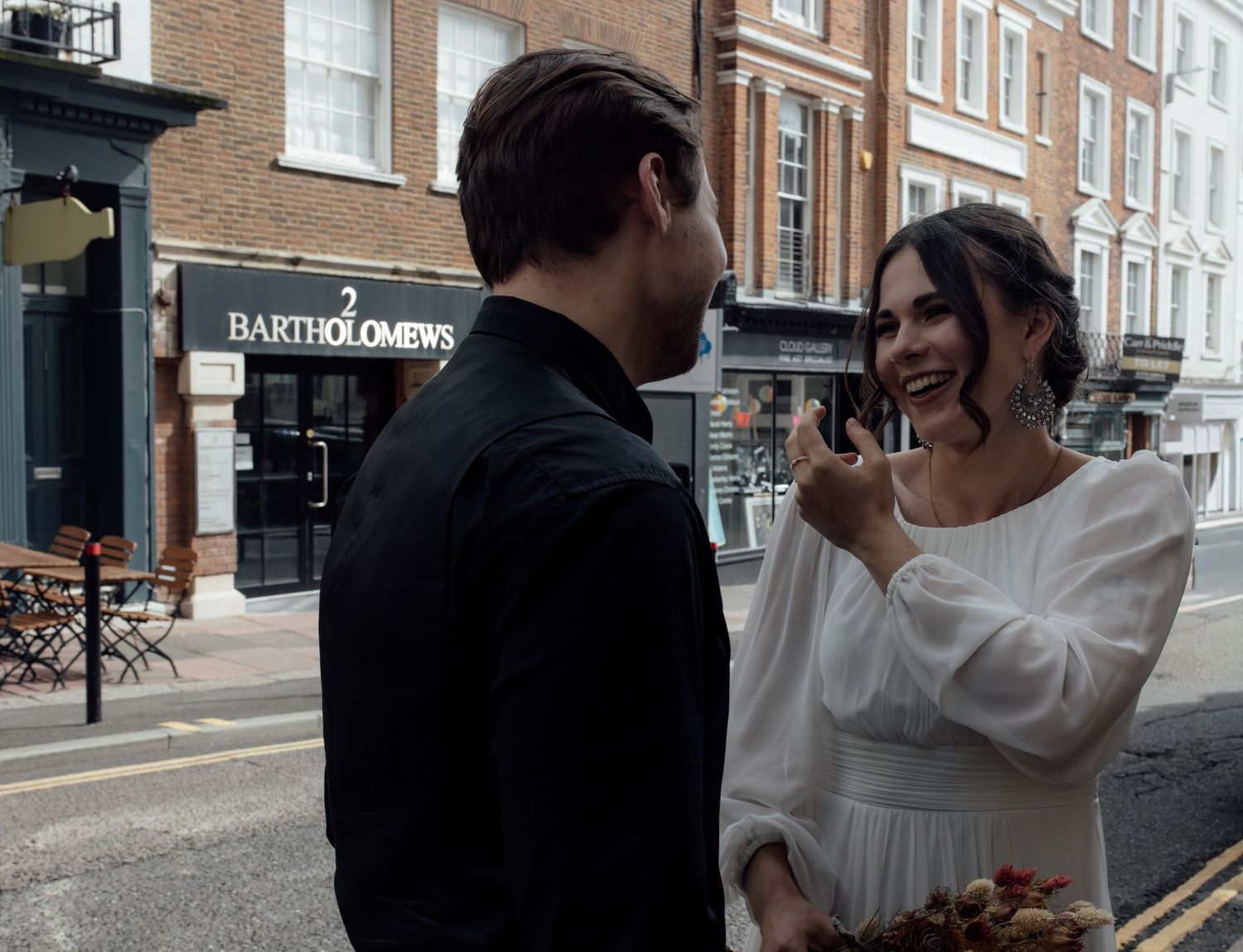 A couple laugh together on a city street corner with brick buildings in the background.