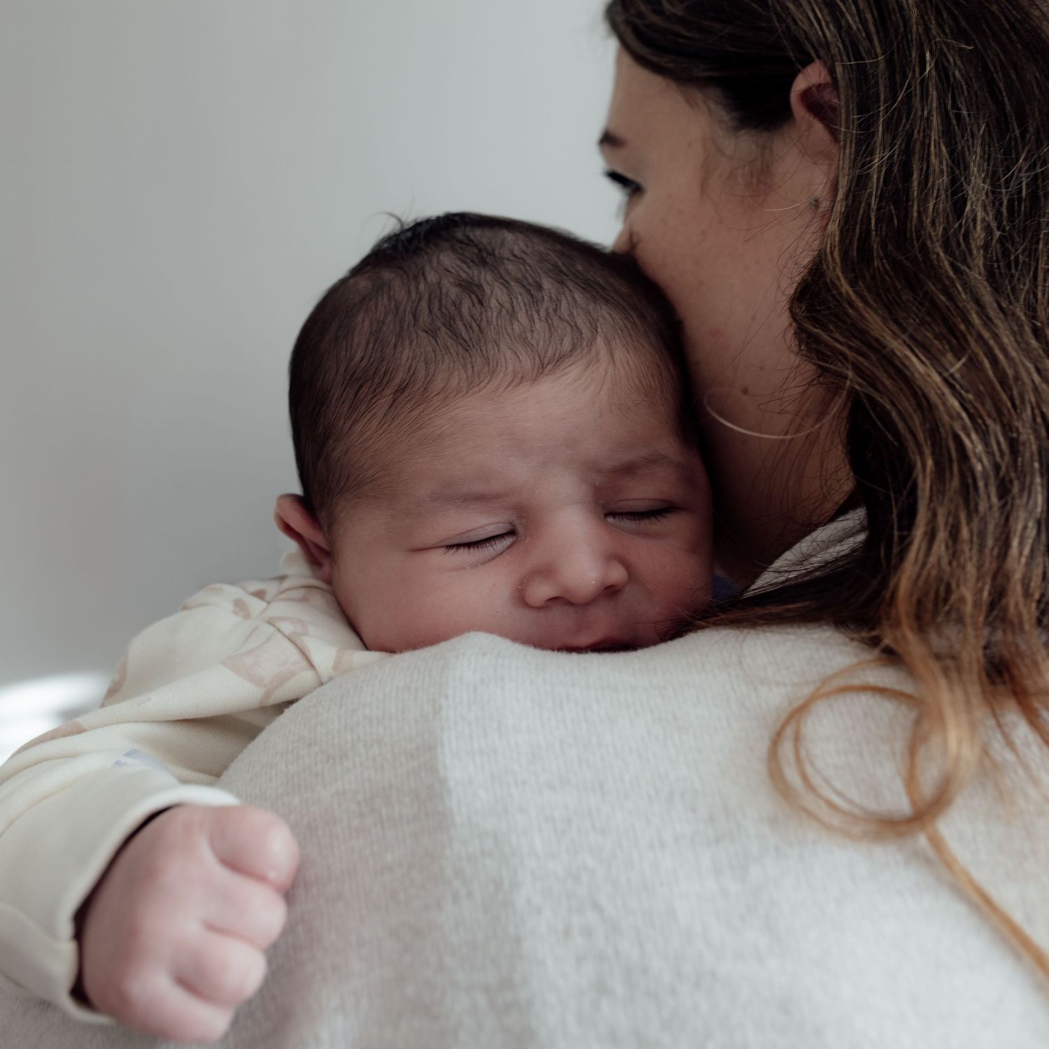 A tender moment between parent and sleeping newborn baby in a soft white setting.