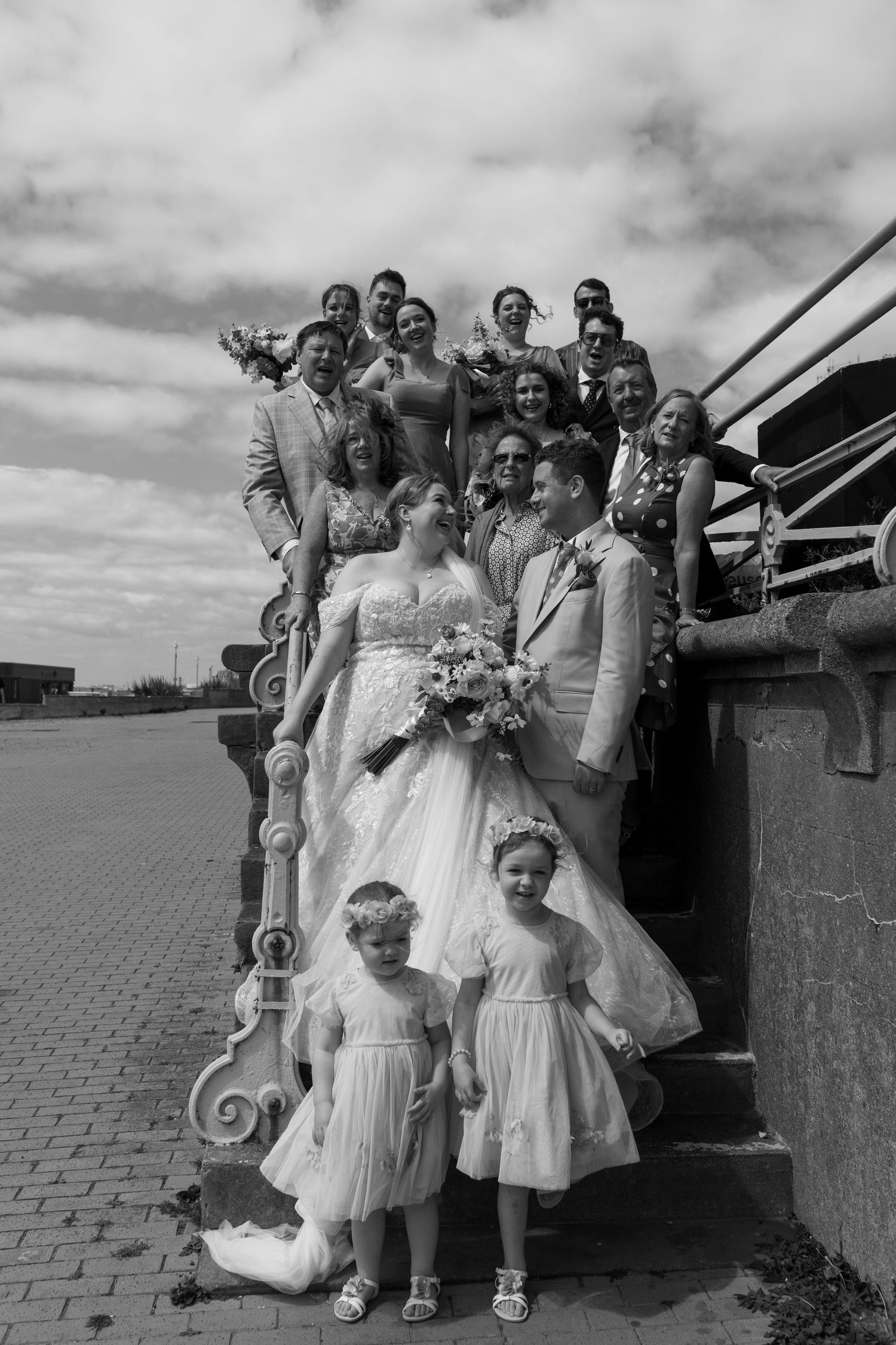 Black and white wedding photo showing a wedding party posing on ornate stone steps outdoors.