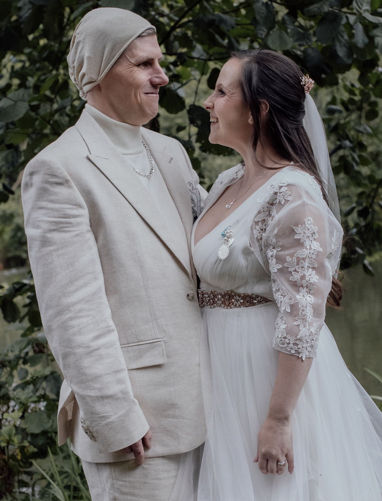 A joyful couple shares a candid moment together outdoors during their wedding celebration in lace and linen attire.