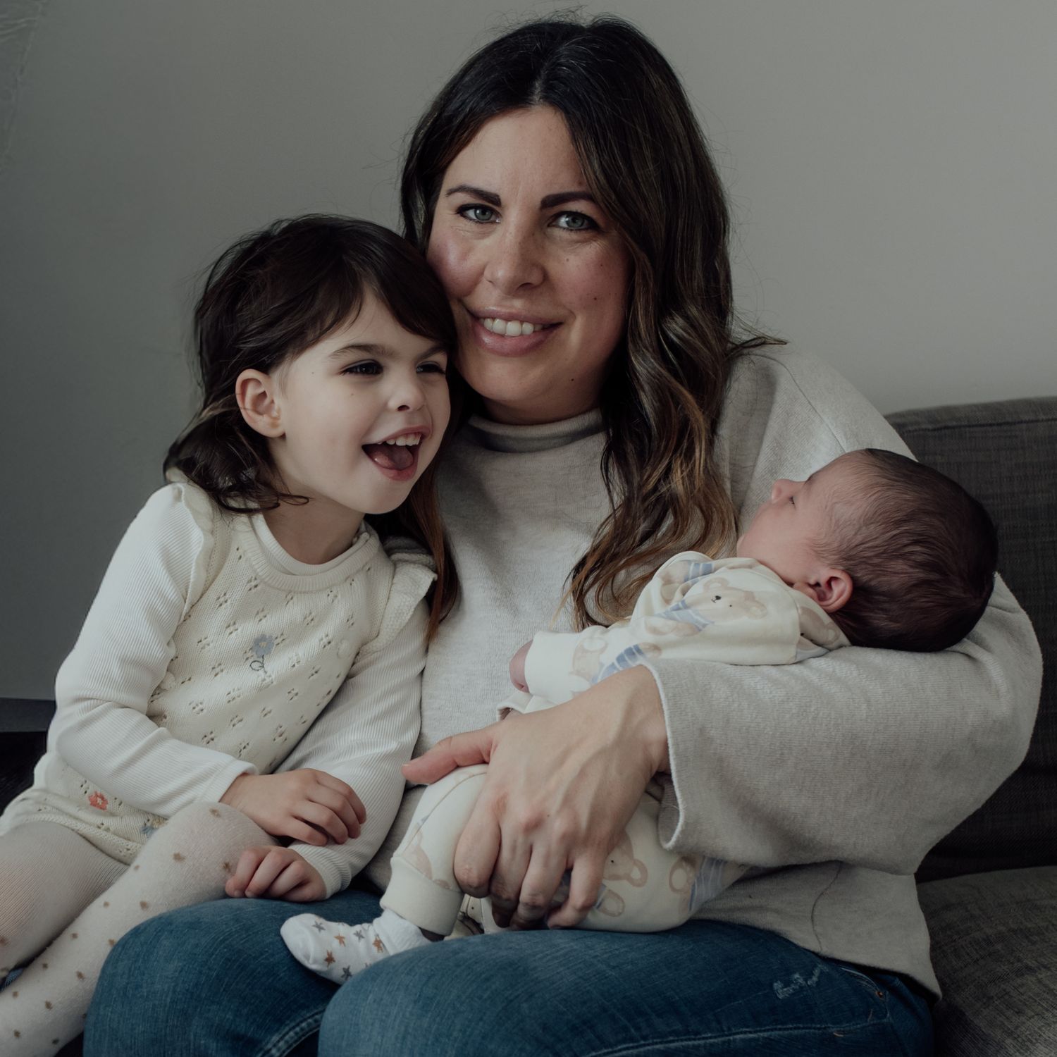 Parent and children share tender moments together while relaxing on a couch in matching cream sweaters.