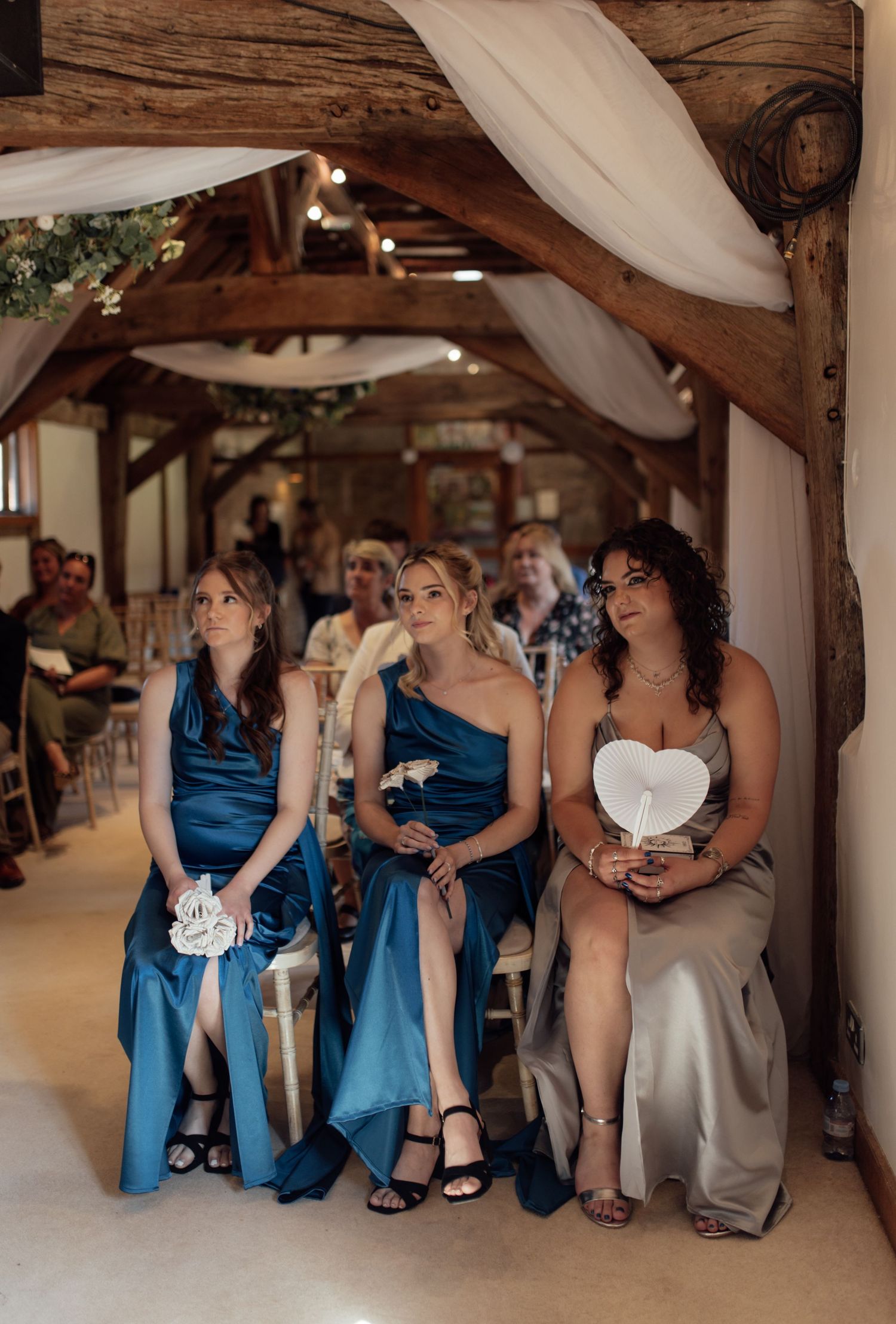 Wedding party members in blue dresses gather together under rustic wooden beams during a celebration.