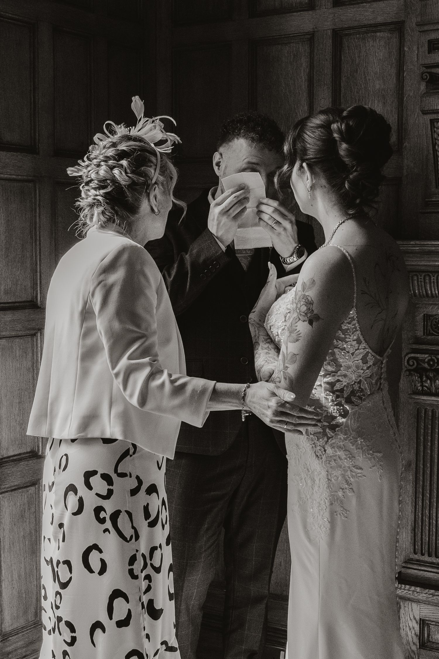Groom crying at his wedding ceremony standing by bride and mother.