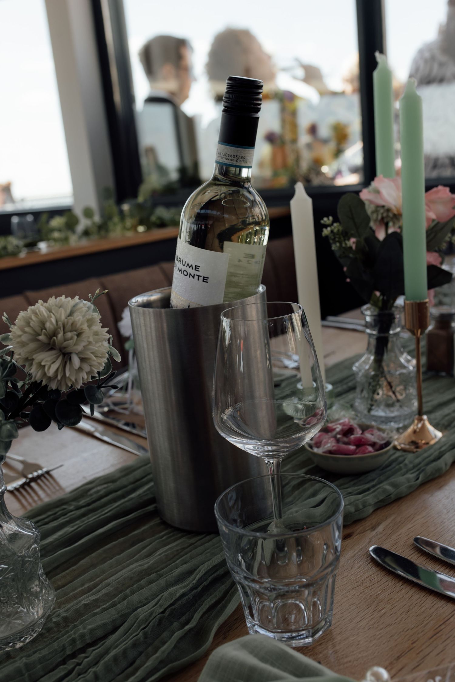 Elegant table setting with wine glasses, flowers, and green palm fronds arranged on a wooden surface for a special occasion.