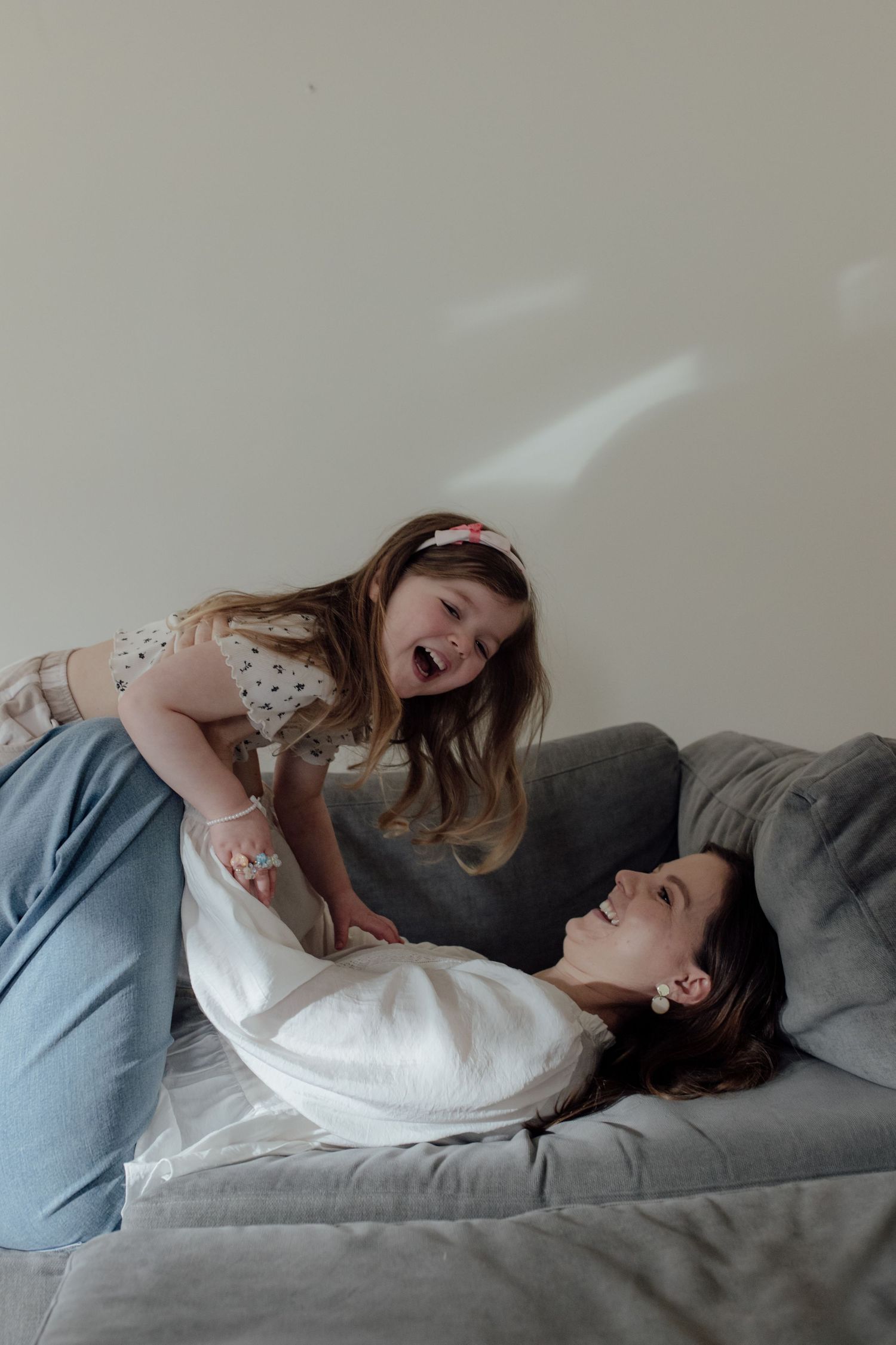 A mum and daughter shares an intimate moment while lying together on a gray couch.