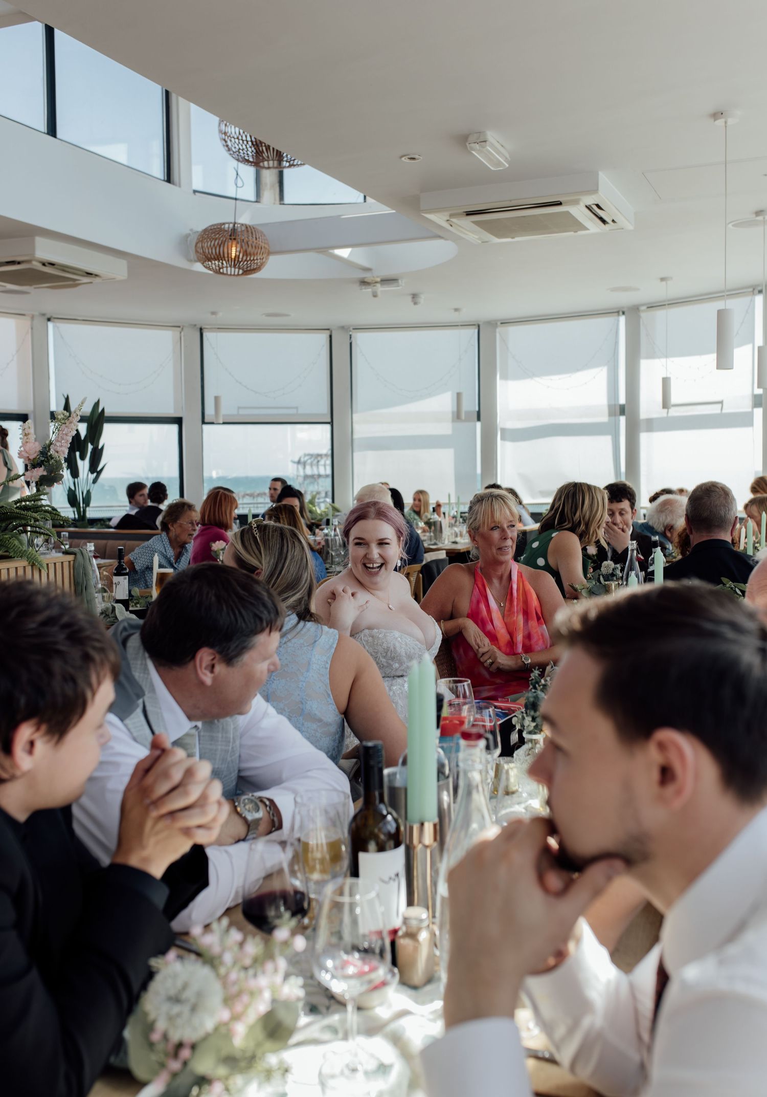 Wedding guests enjoying drinks and conversation at a bright reception venue with panoramic windows.