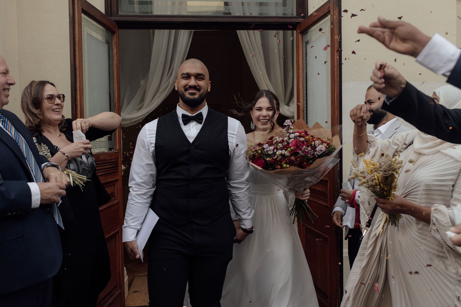 Wedding guests toss rose petals in celebration as newlyweds exit the church after their ceremony.