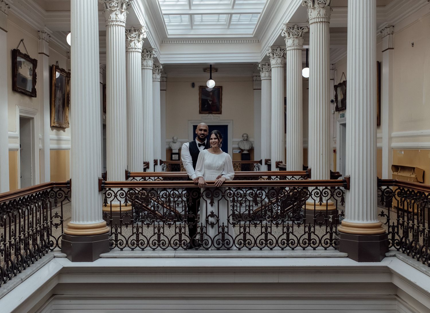 Interior panorama of a historic building with white columns and ornate iron railings along an upper balcony level.