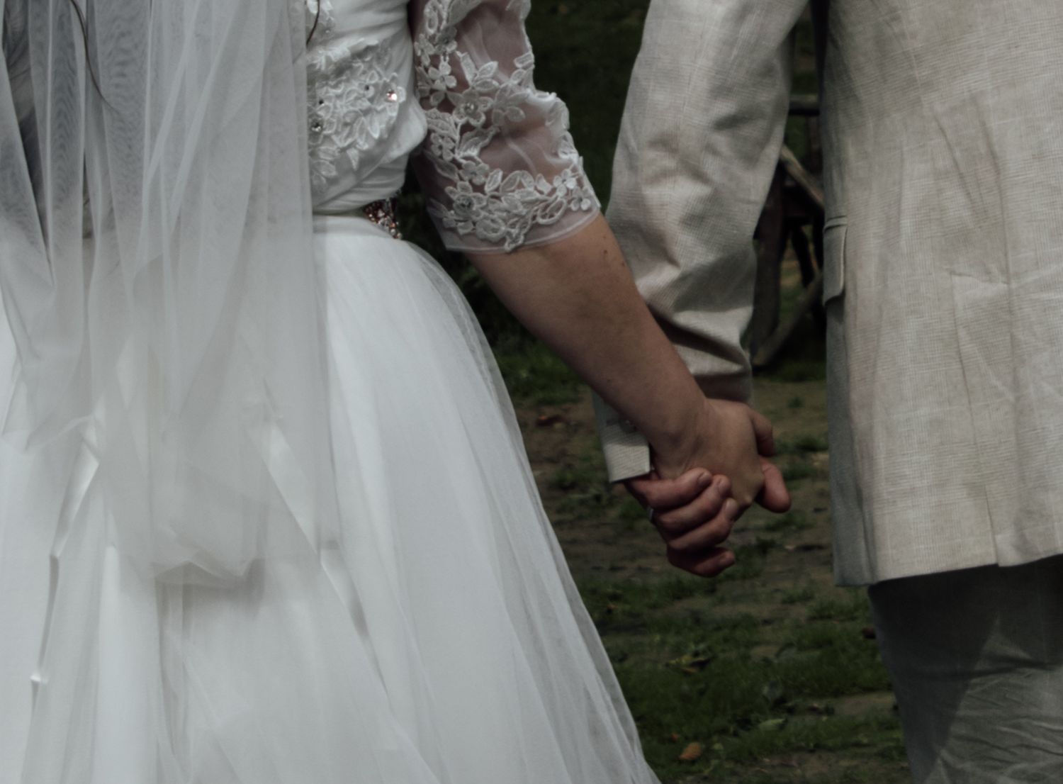 Close-up of newlywed couple holding hands, with bride wearing white wedding dress and groom in light colored suit.