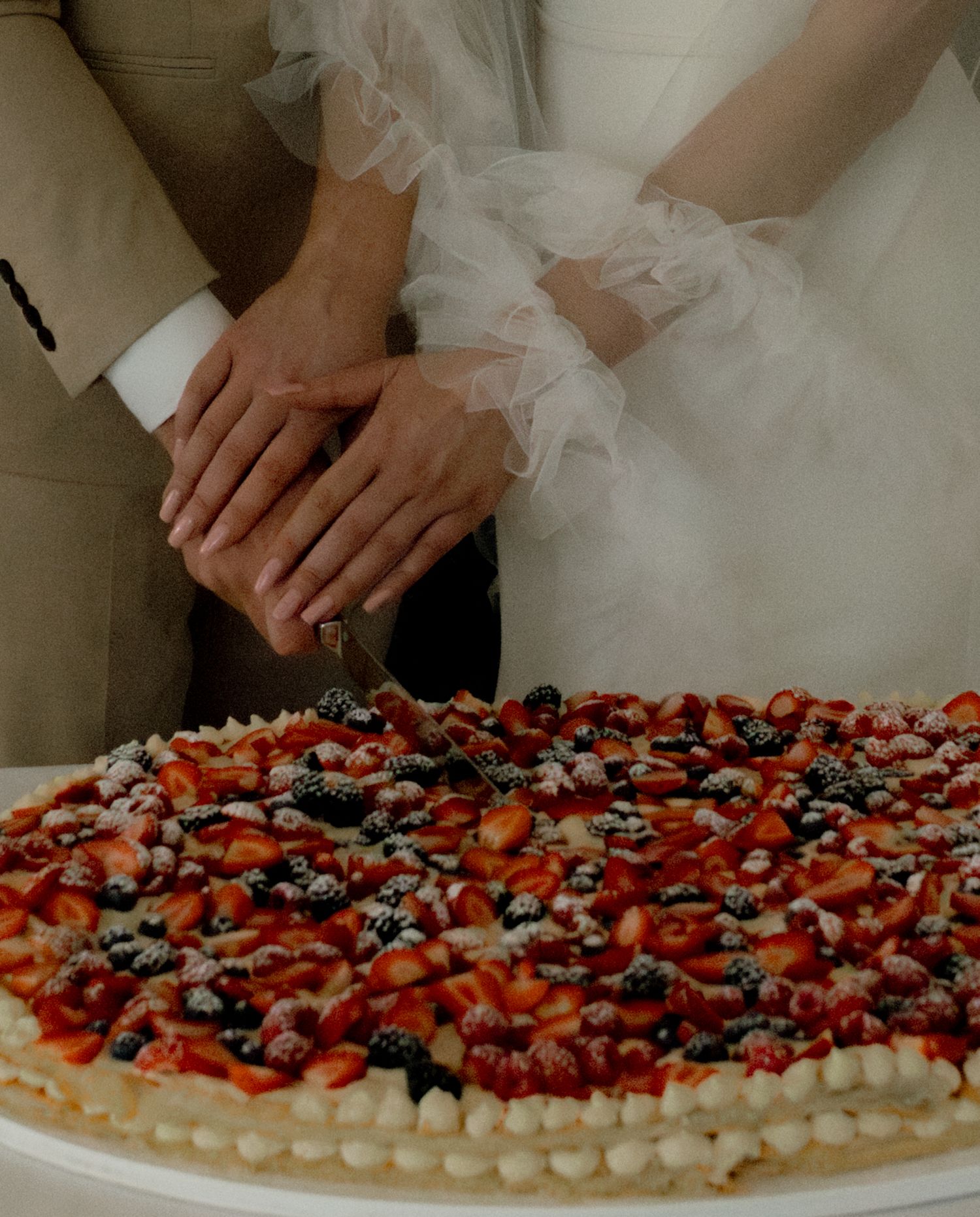 Closeup of hands arranging colorful fresh berries on a round decorated dessert.