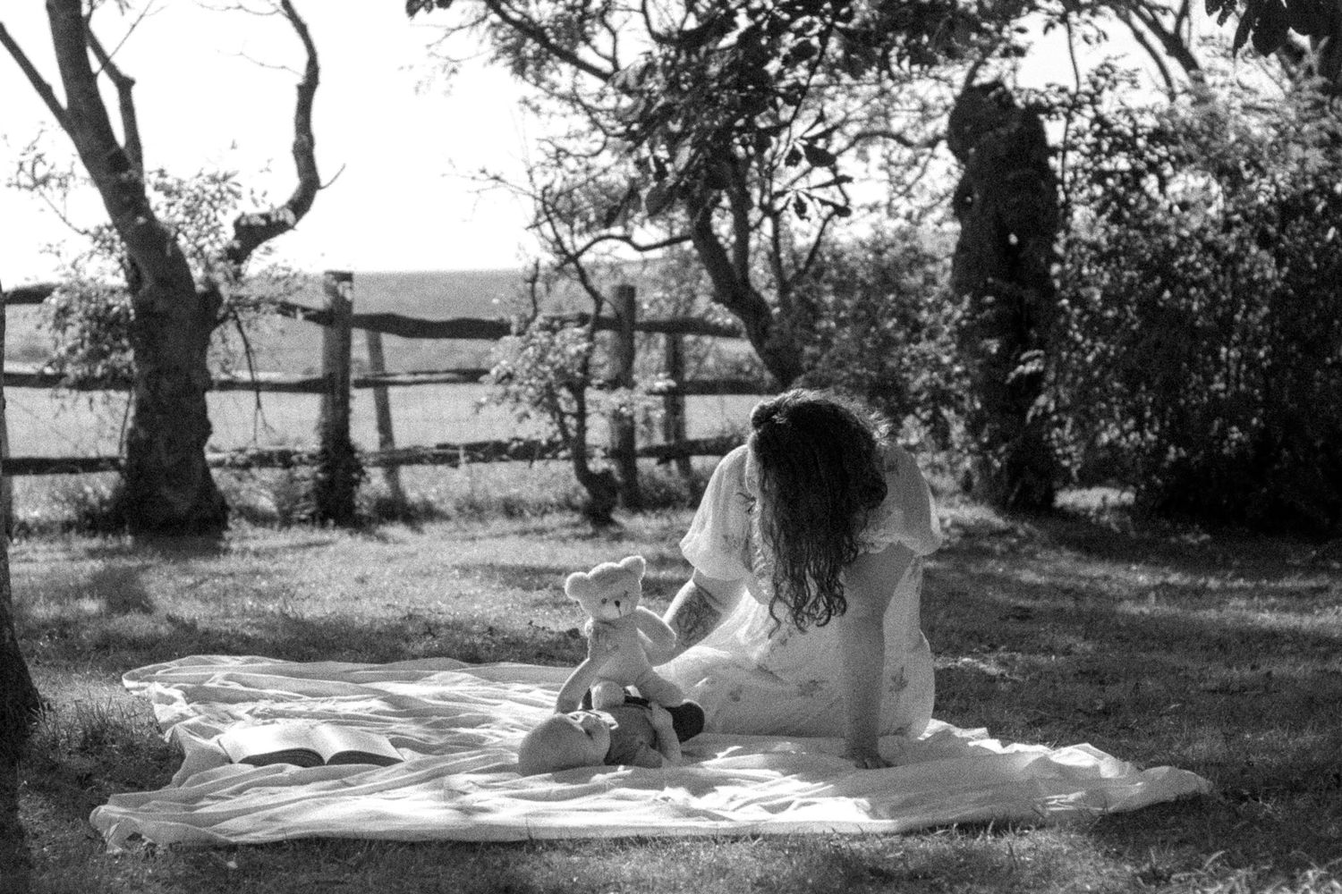 A figure in a white dress sits on a blanket writing in a journal outdoors in a black and white photograph.