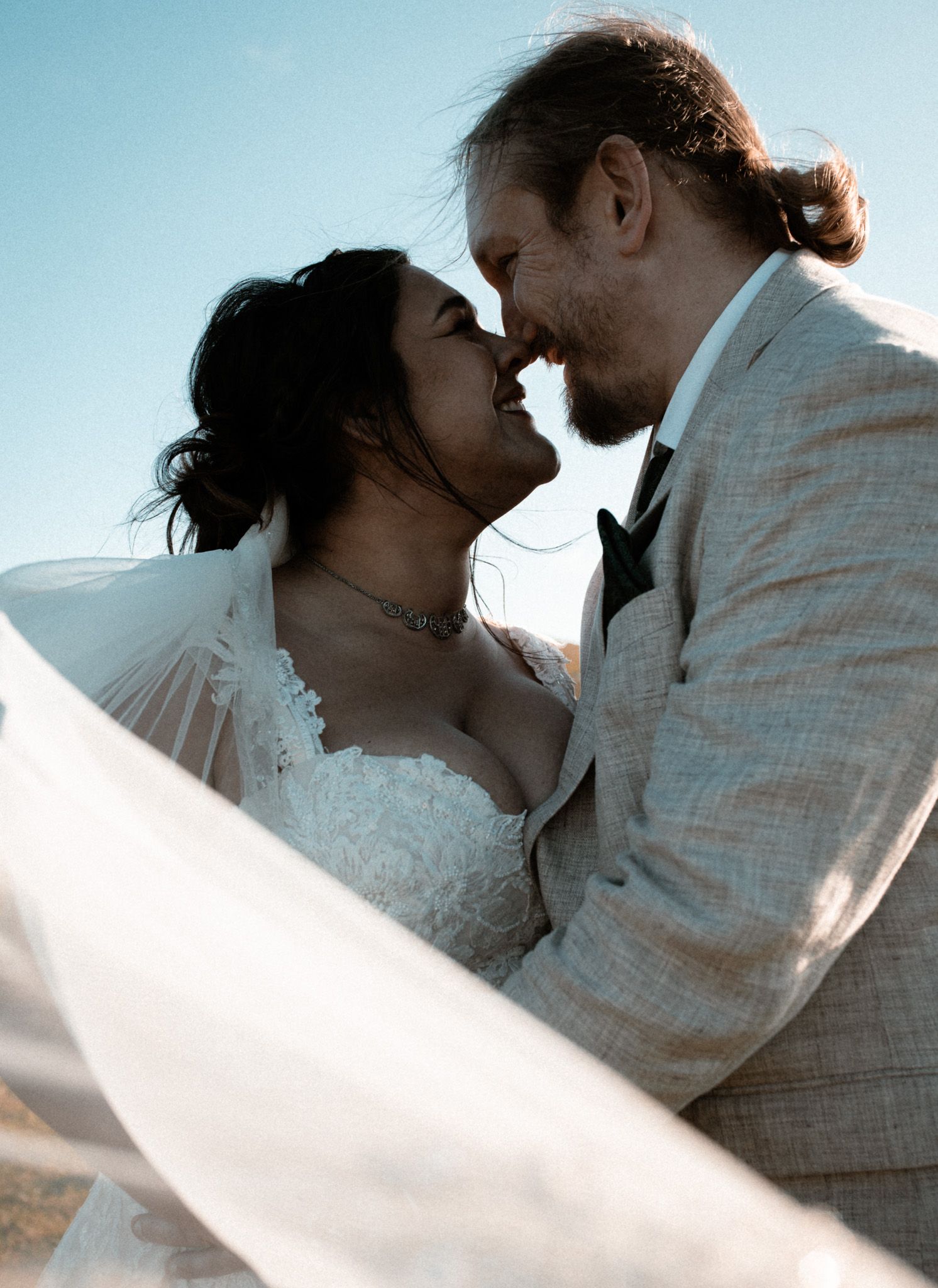 A romantic couple in white clothing embrace and nearly kiss against a light blue sky in a series of dreamy photos.