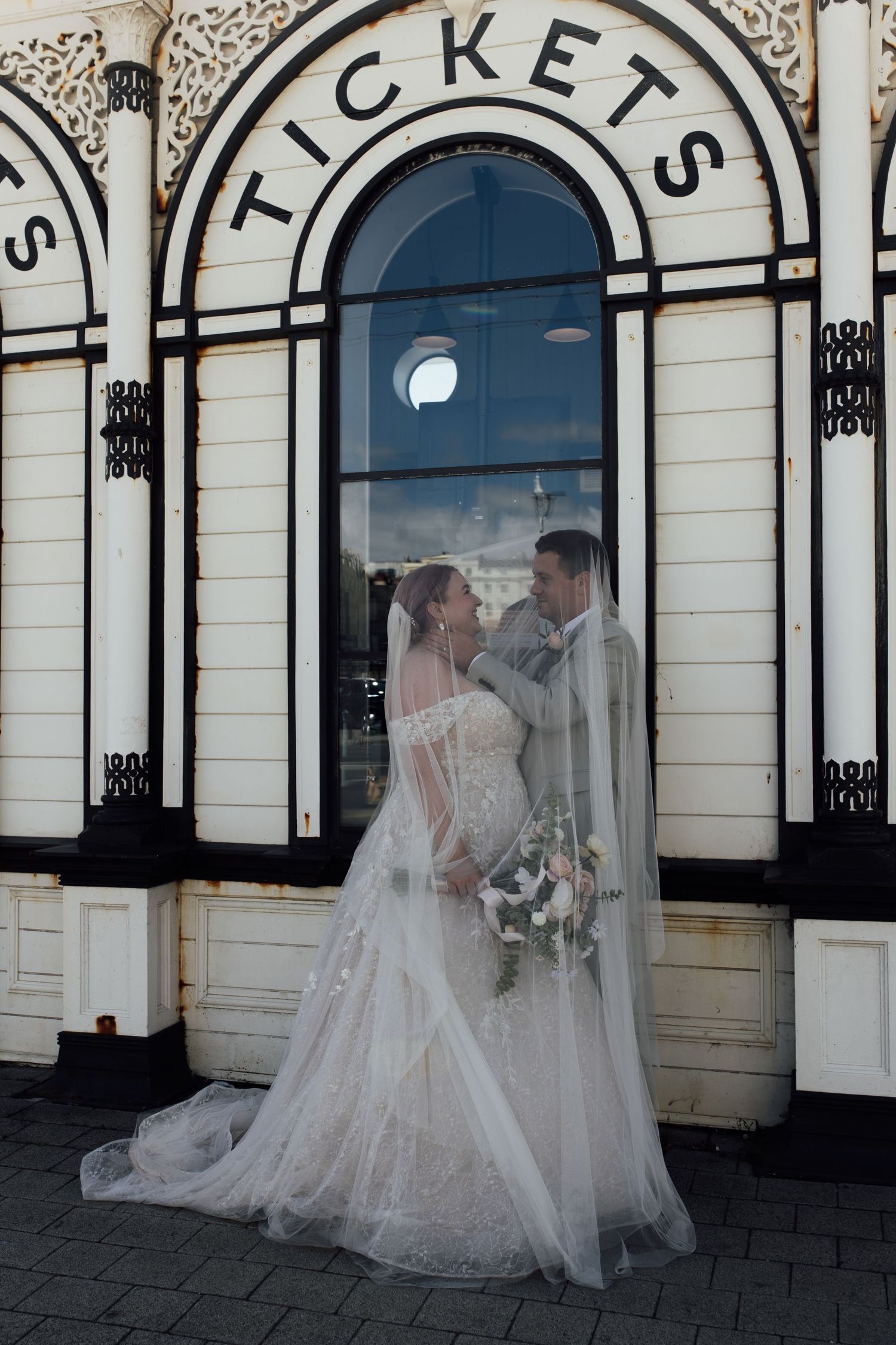 Bride and groom stand under veil looking at each other.