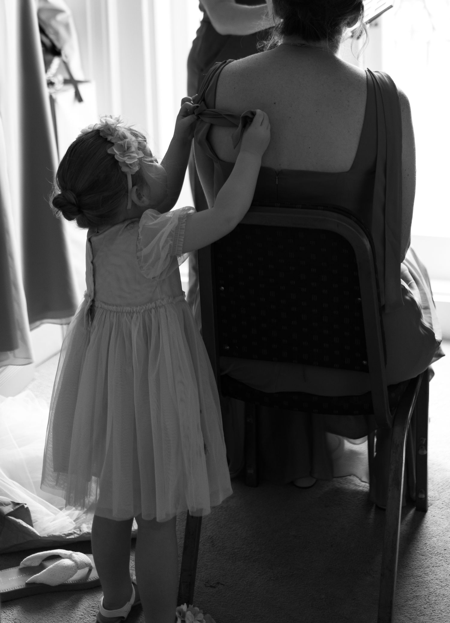 A series of black and white photos showing a child in a dress and adults in silhouette against a bright window.